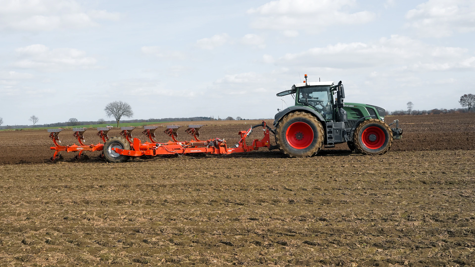 Green tractor plowing a brown field under a cloudy sky