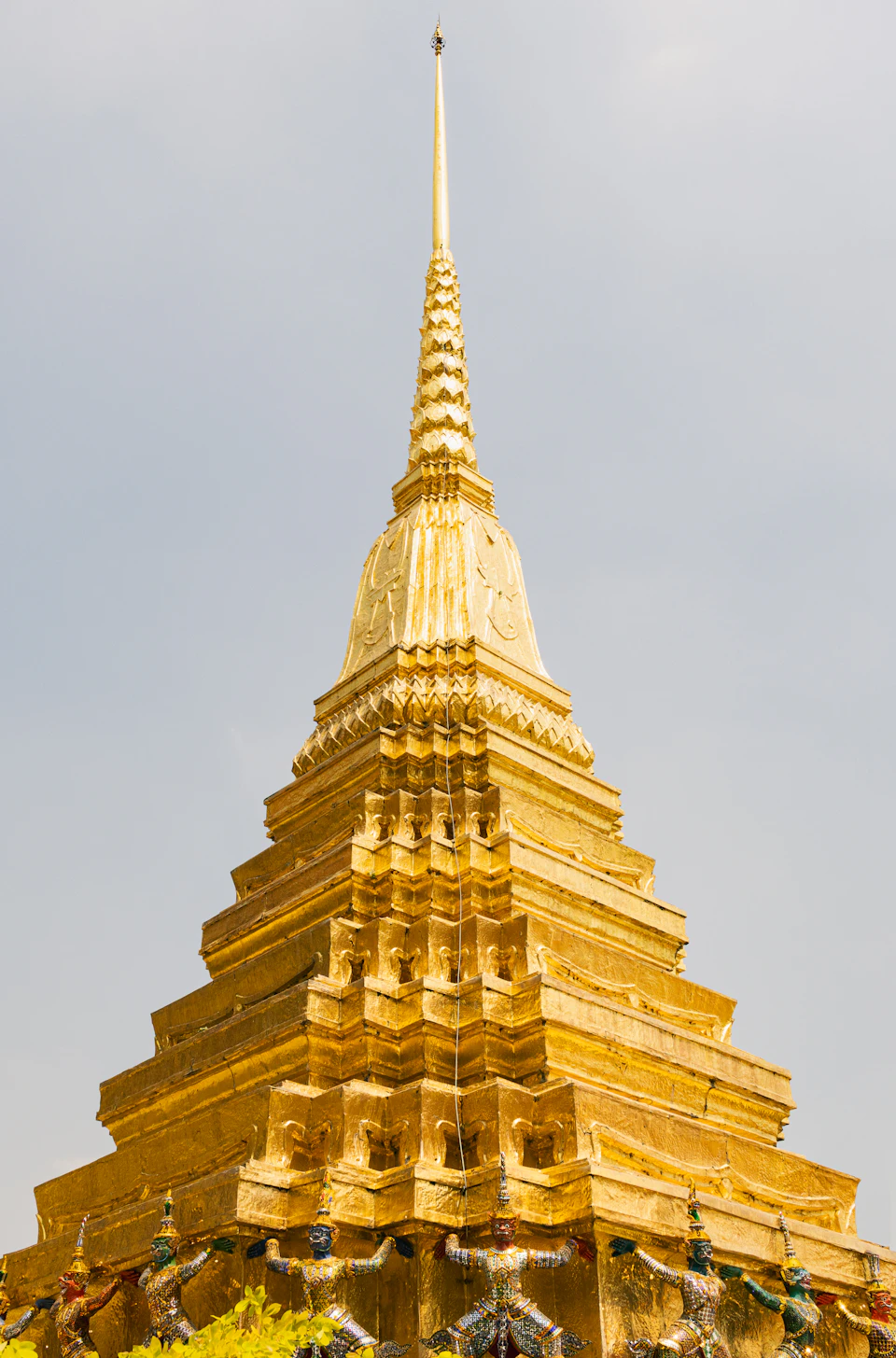 Tall, golden-colored temple with multiple levels and spires rising above the hillside landscape
