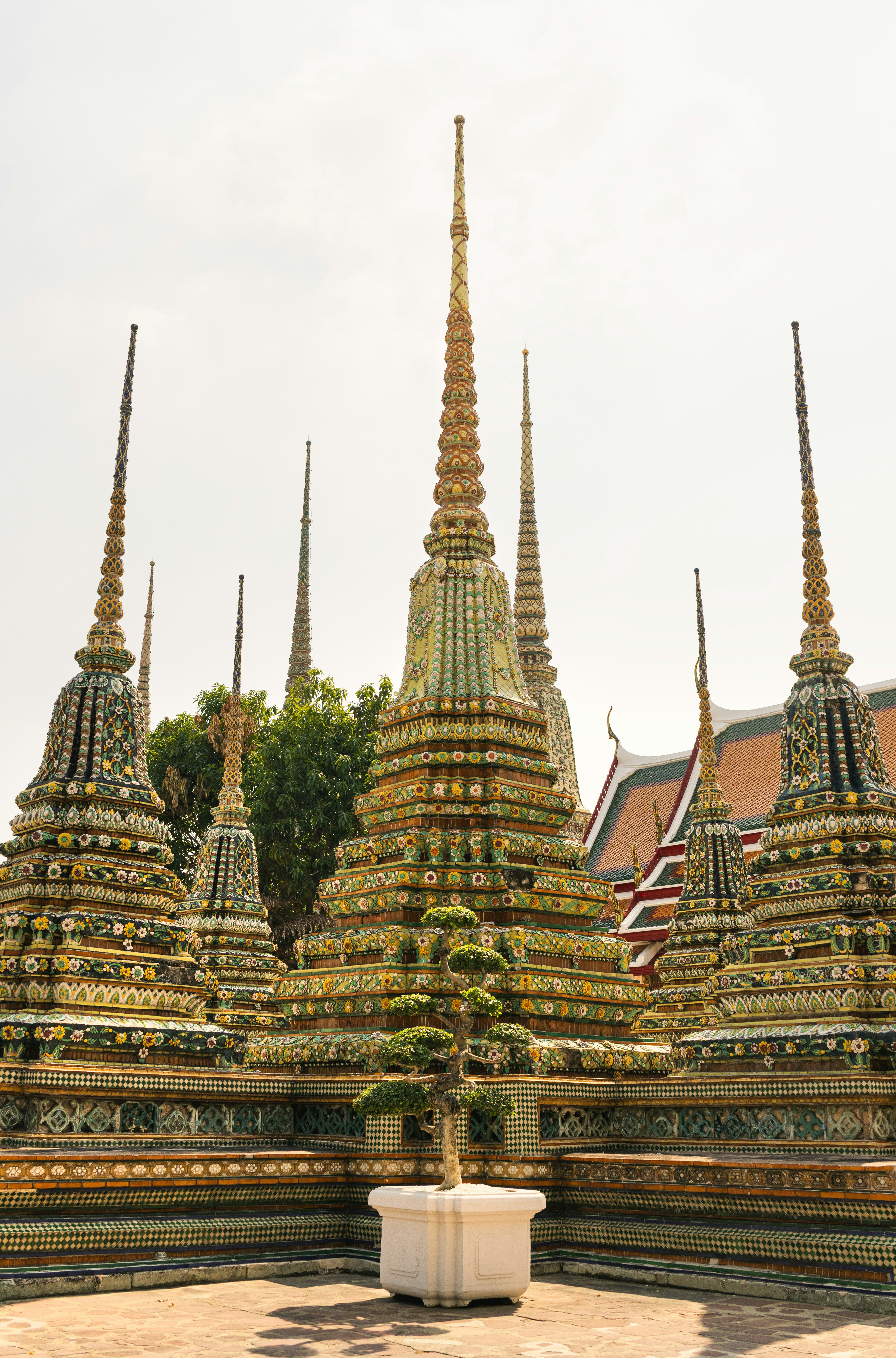 Estupas ornamentadas y un árbol en maceta en el patio de un templo.