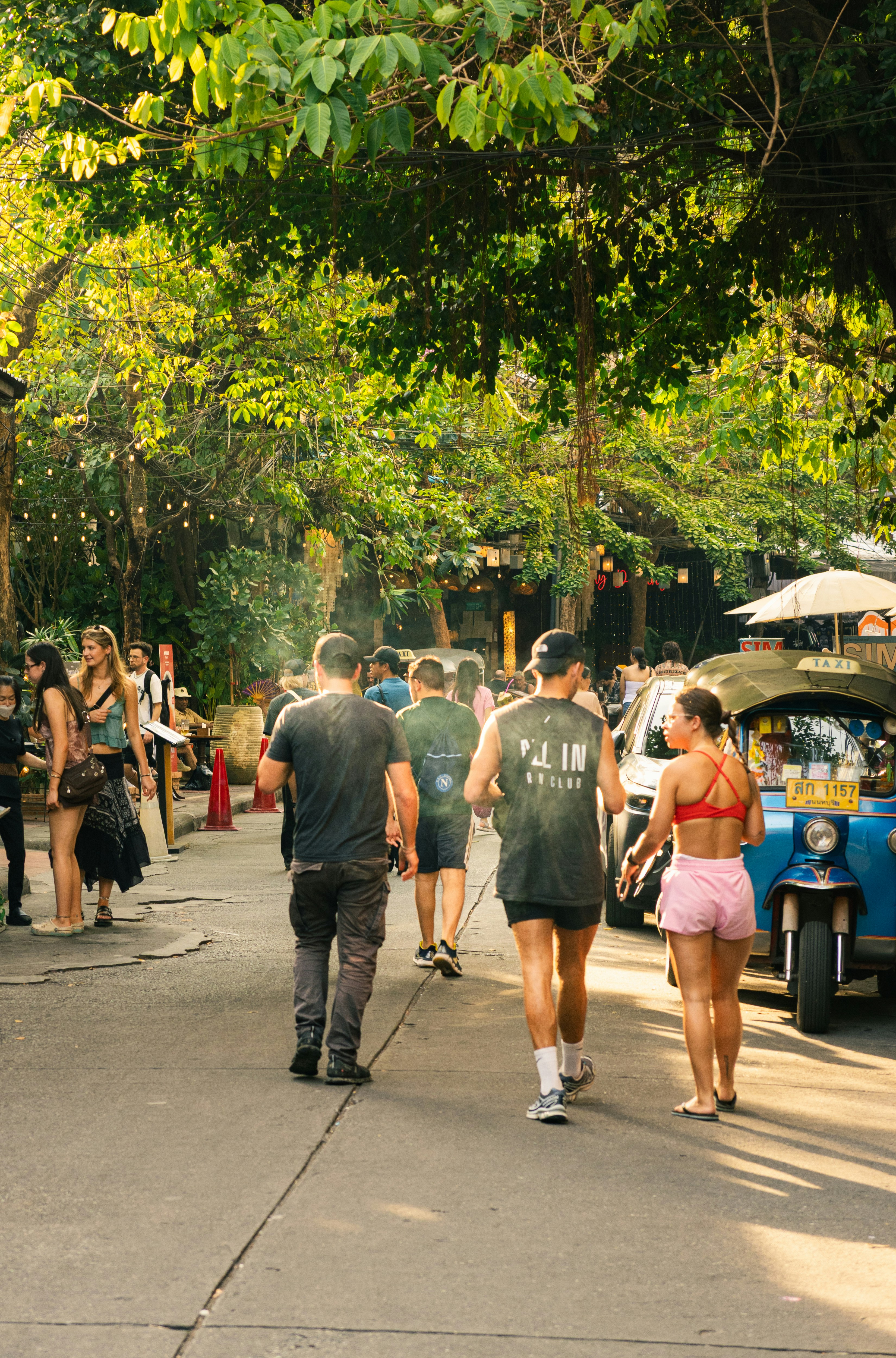 Gente caminando por una calle con árboles y un tuk-tuk