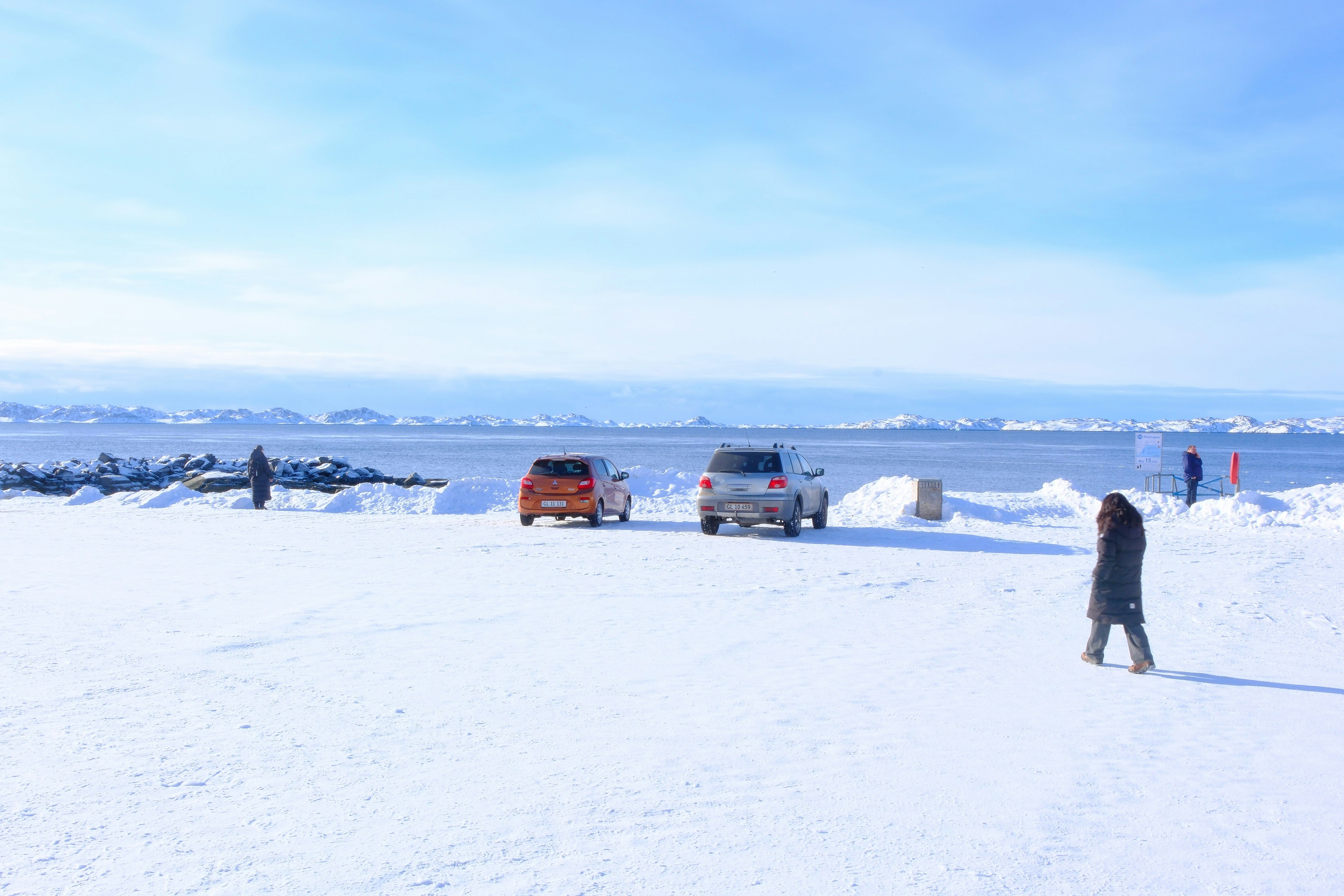 Dois carros estacionados em uma paisagem nevada à beira do oceano.