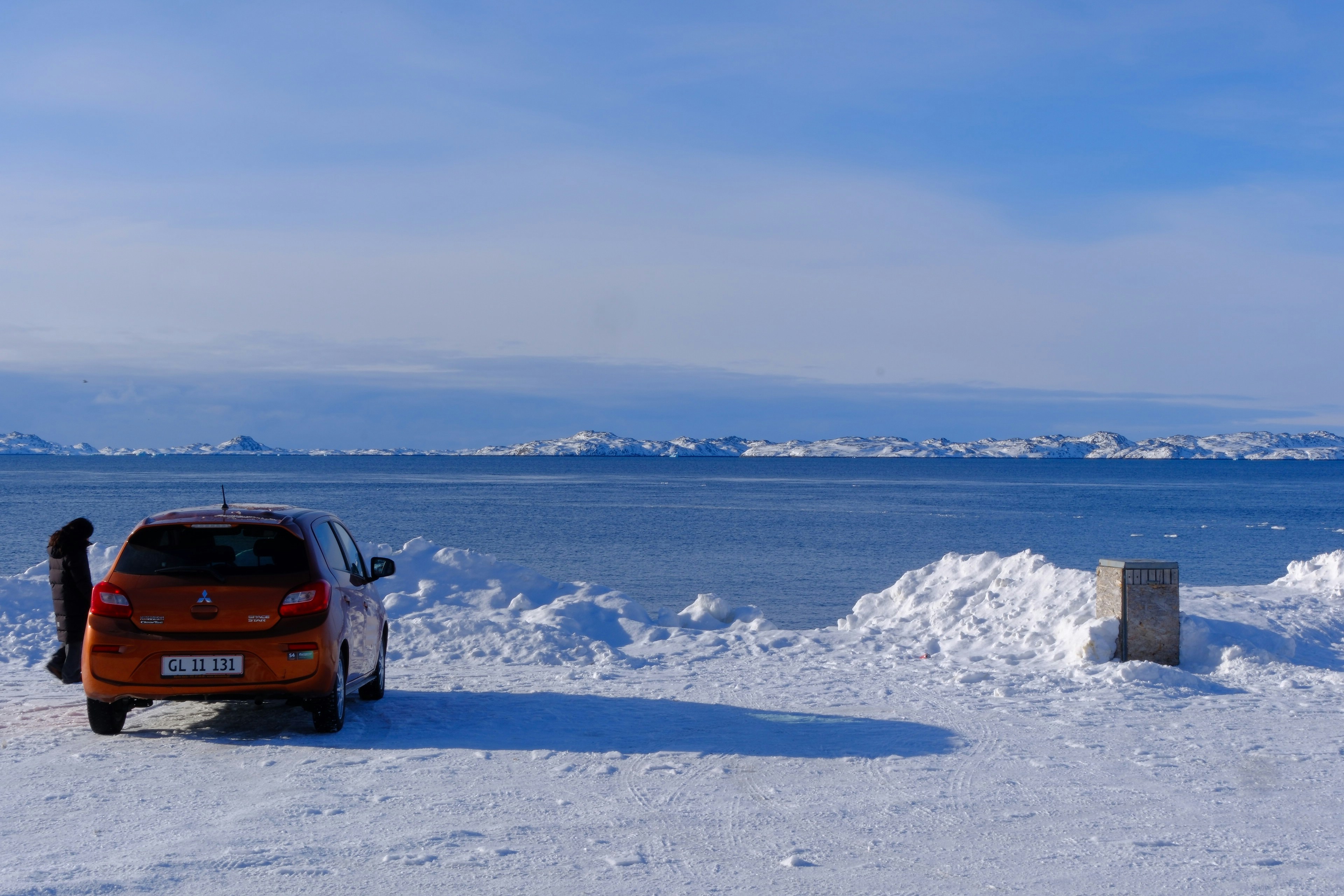 Carro laranja estacionado na praia nevada com vista gelada para o oceano