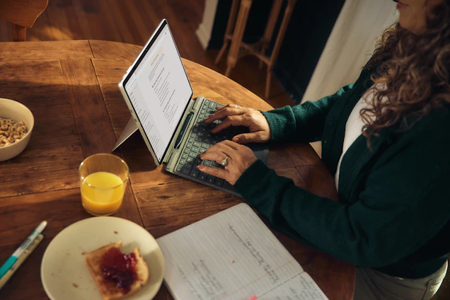 Woman typing on laptop at wooden table with breakfast.