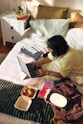 Woman working on laptop on bed with snacks and books.
