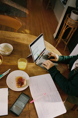 Person working on laptop at wooden table with breakfast