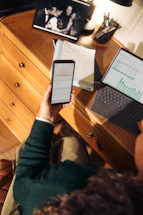 Person holding phone near laptop and tablet on desk