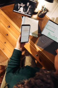 Person holding phone near laptop and tablet on desk