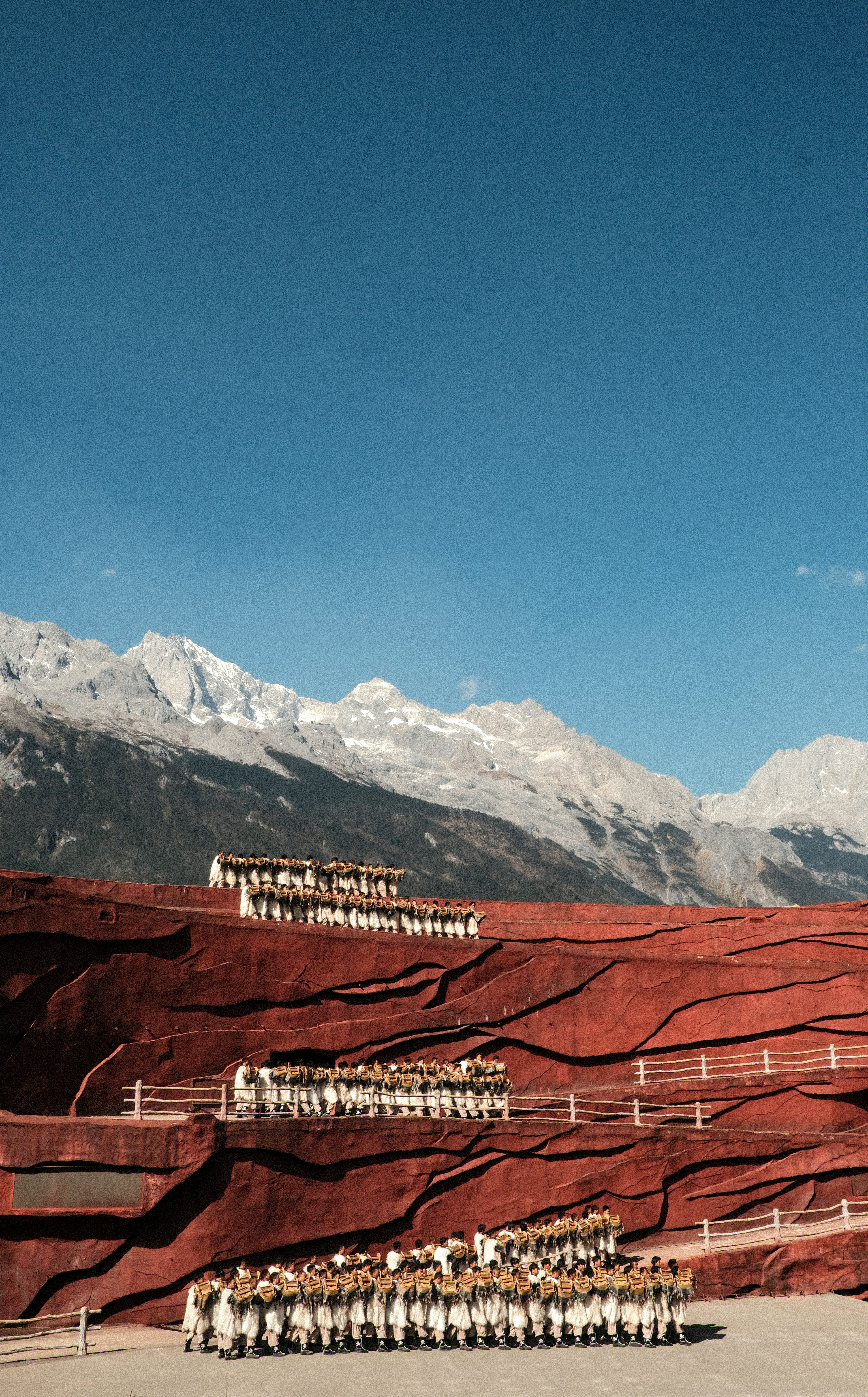 People in traditional dress on red terraces with mountains.