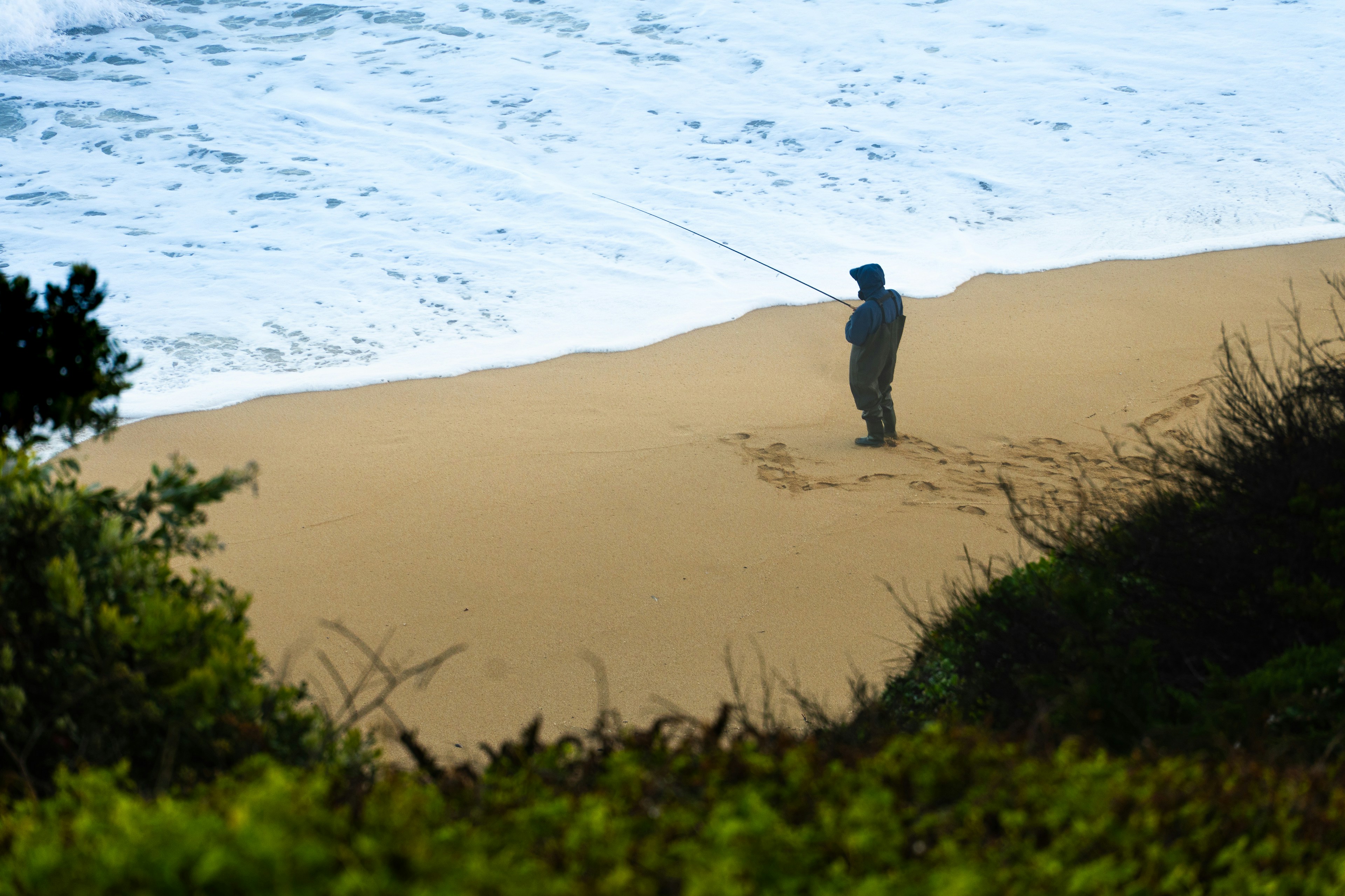 Man fishing on a sandy beach with ocean waves