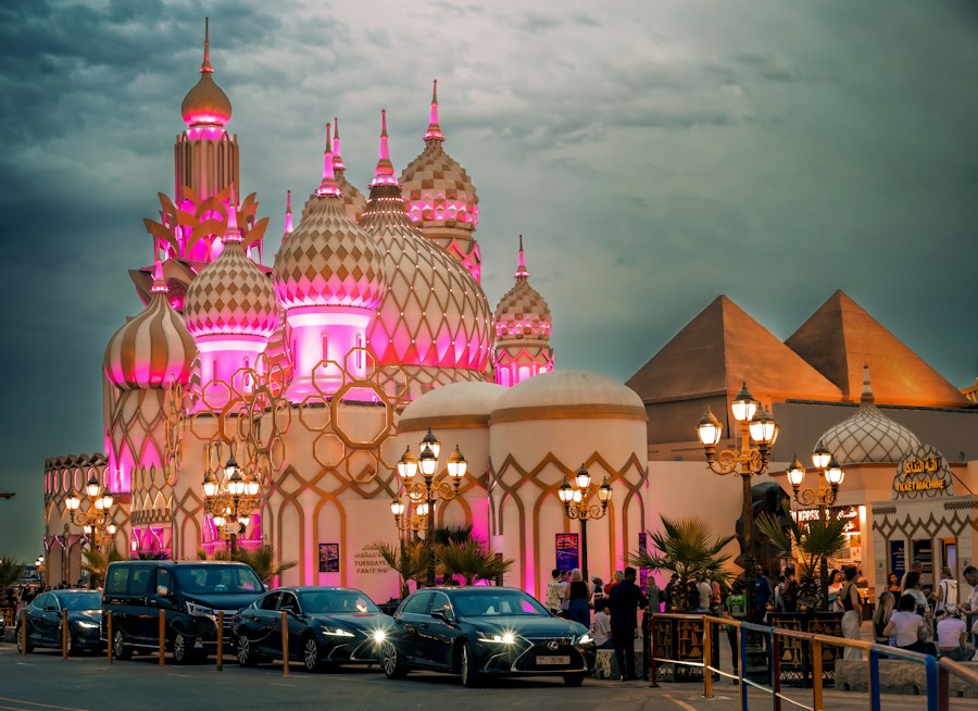 Illuminated pink-and-gold domes of the Global Village Dubai entrance at dusk with visitors walking in