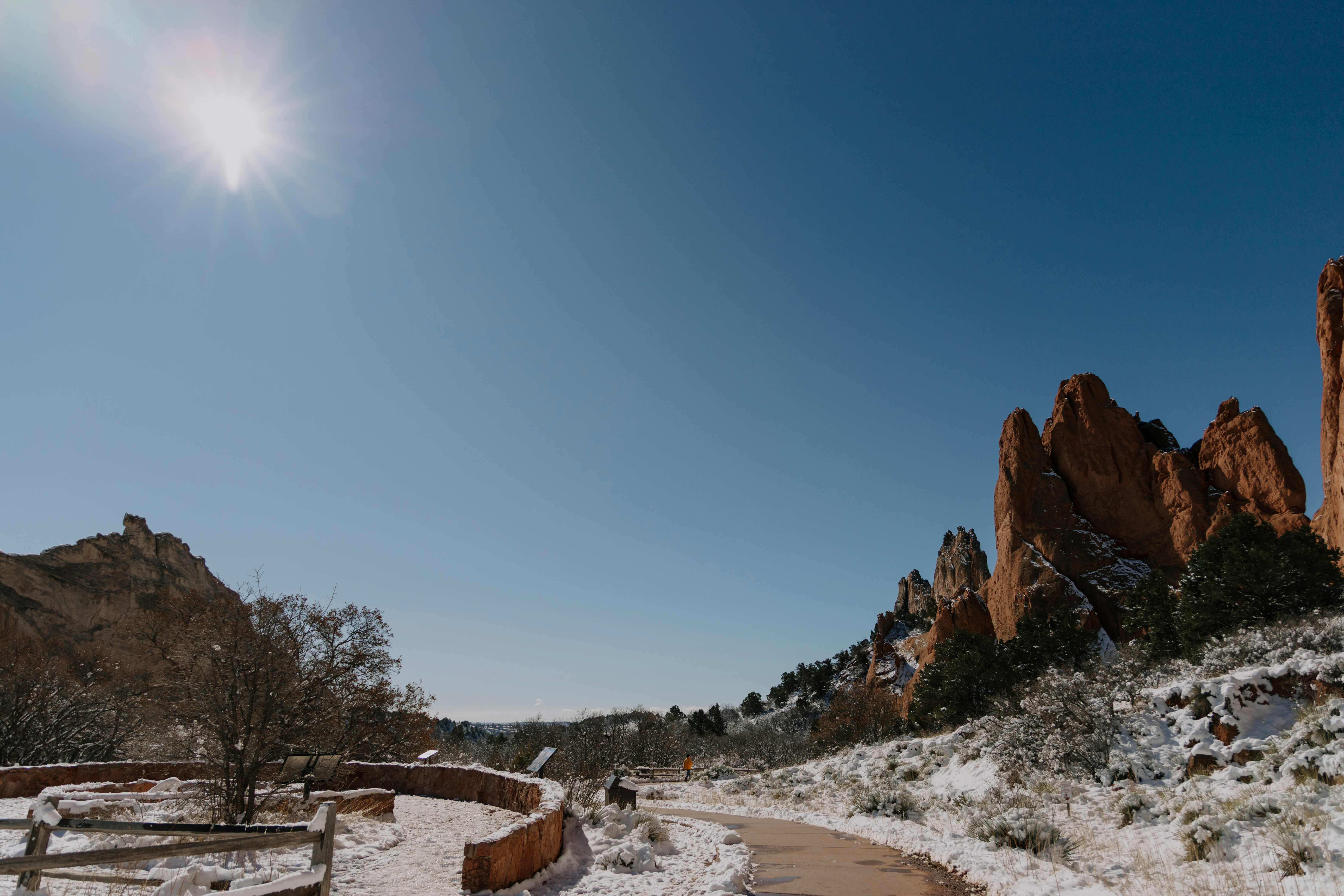 Snowy path leads to red rock formations under clear sky.