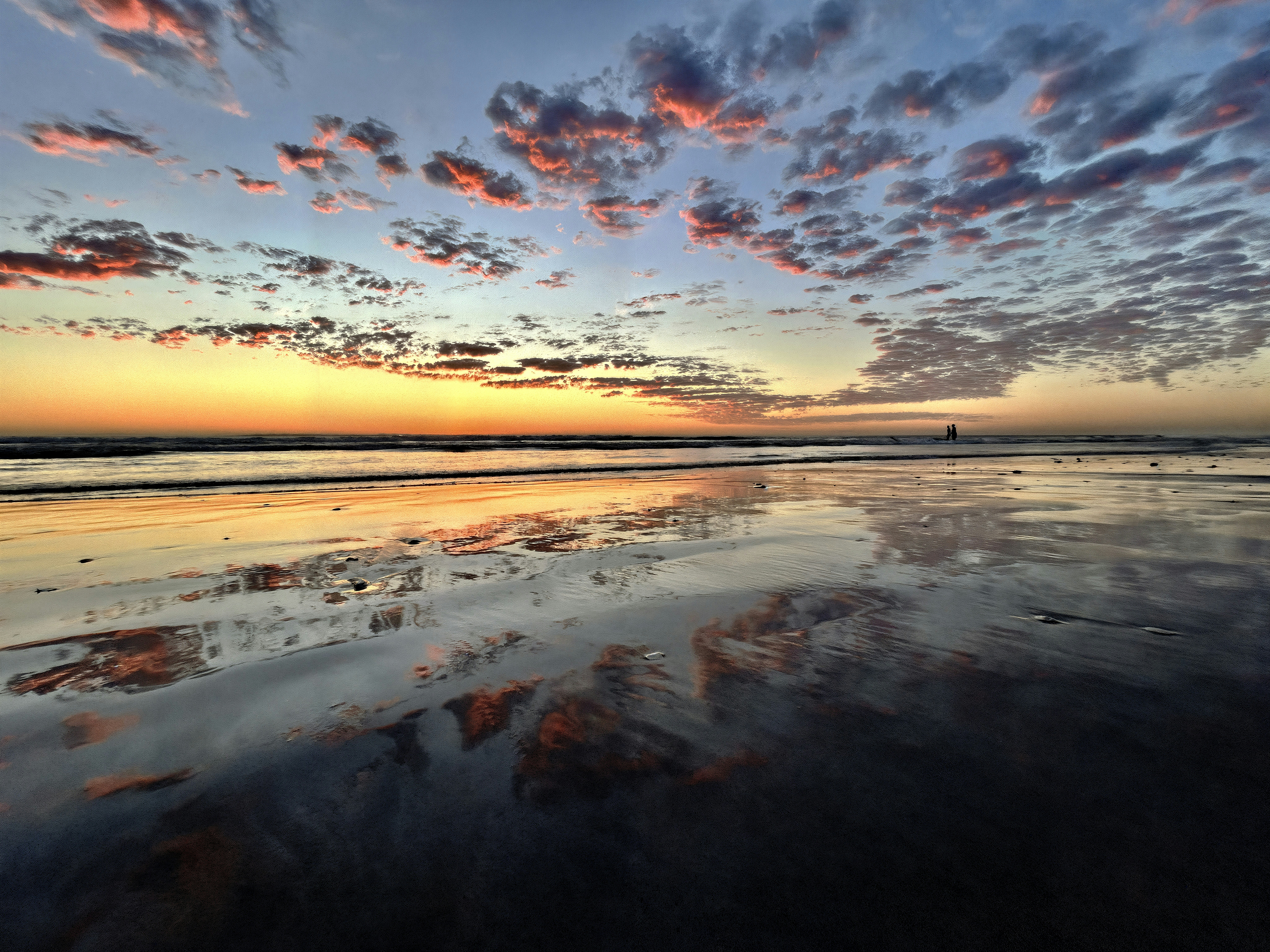 Coucher de soleil se reflétant sur le sable mouillé de la plage.