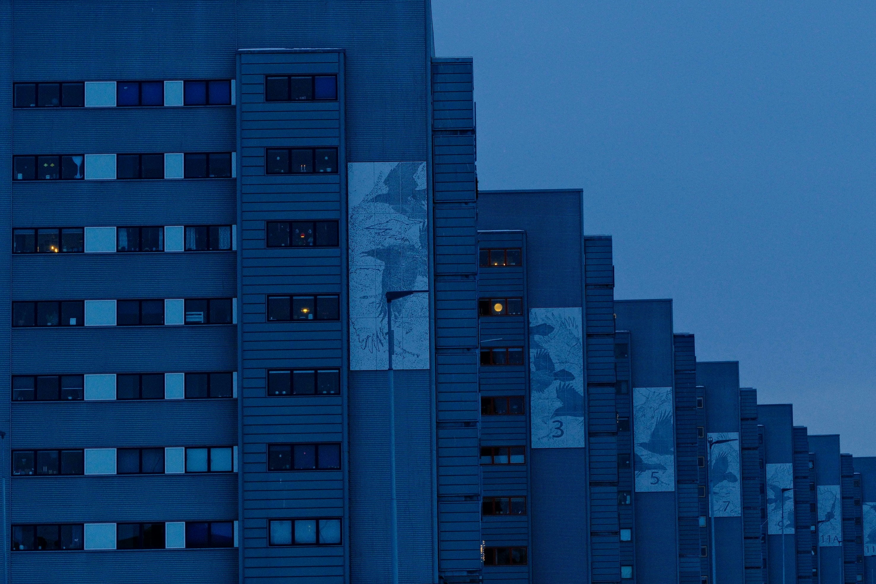 Prédios modernos de apartamentos azuis ao entardecer com janelas iluminadas.