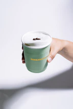 Hand holding a green cup with foamy drink