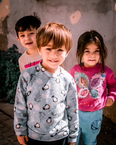 Three young children stand together smiling.