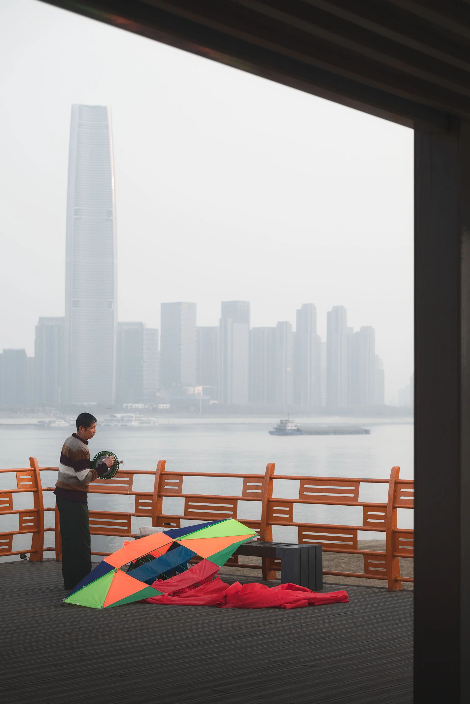 A man on a riverside deck winding a kite line onto a hand reel
