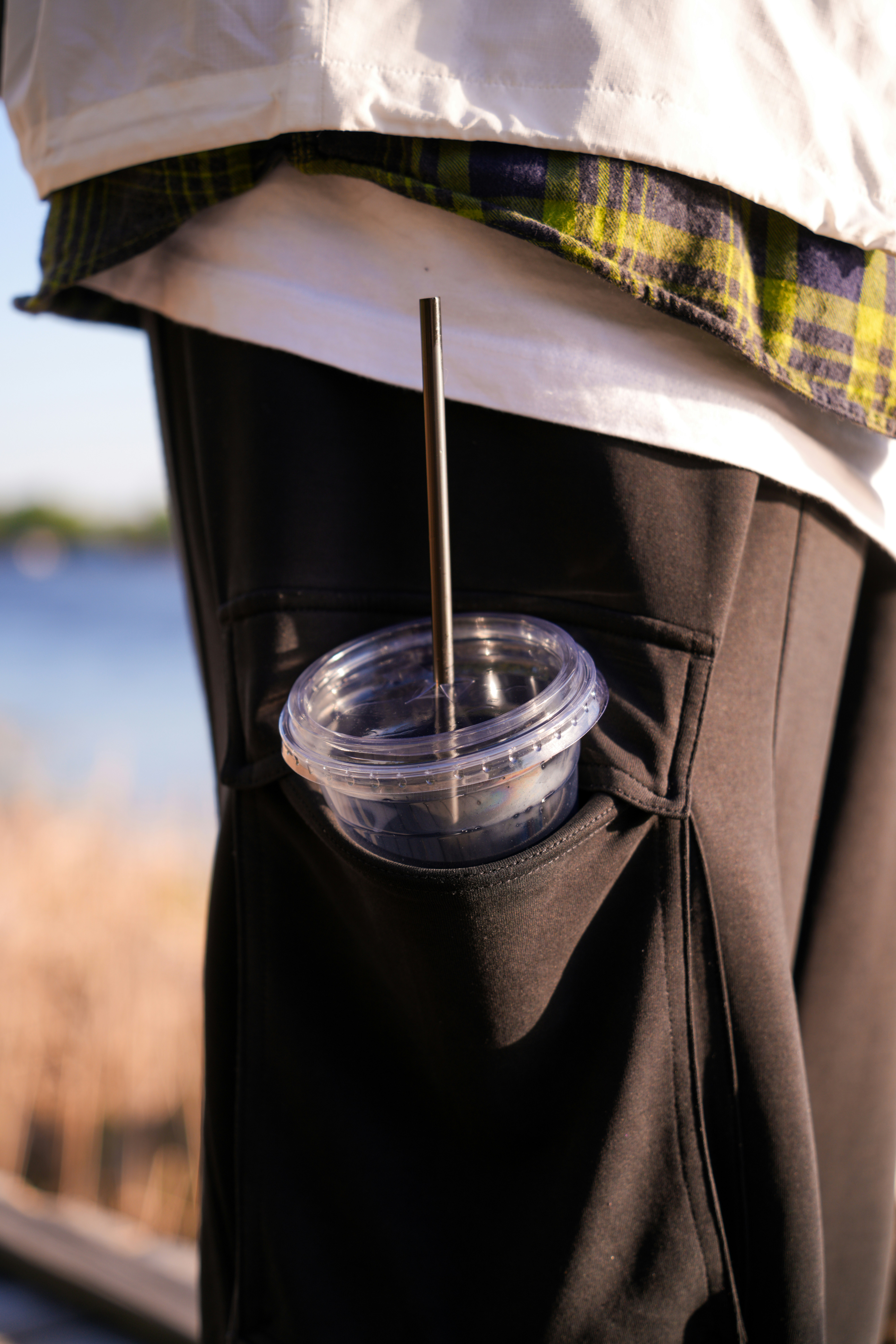 A person's pocket holds a plastic cup with a stick.