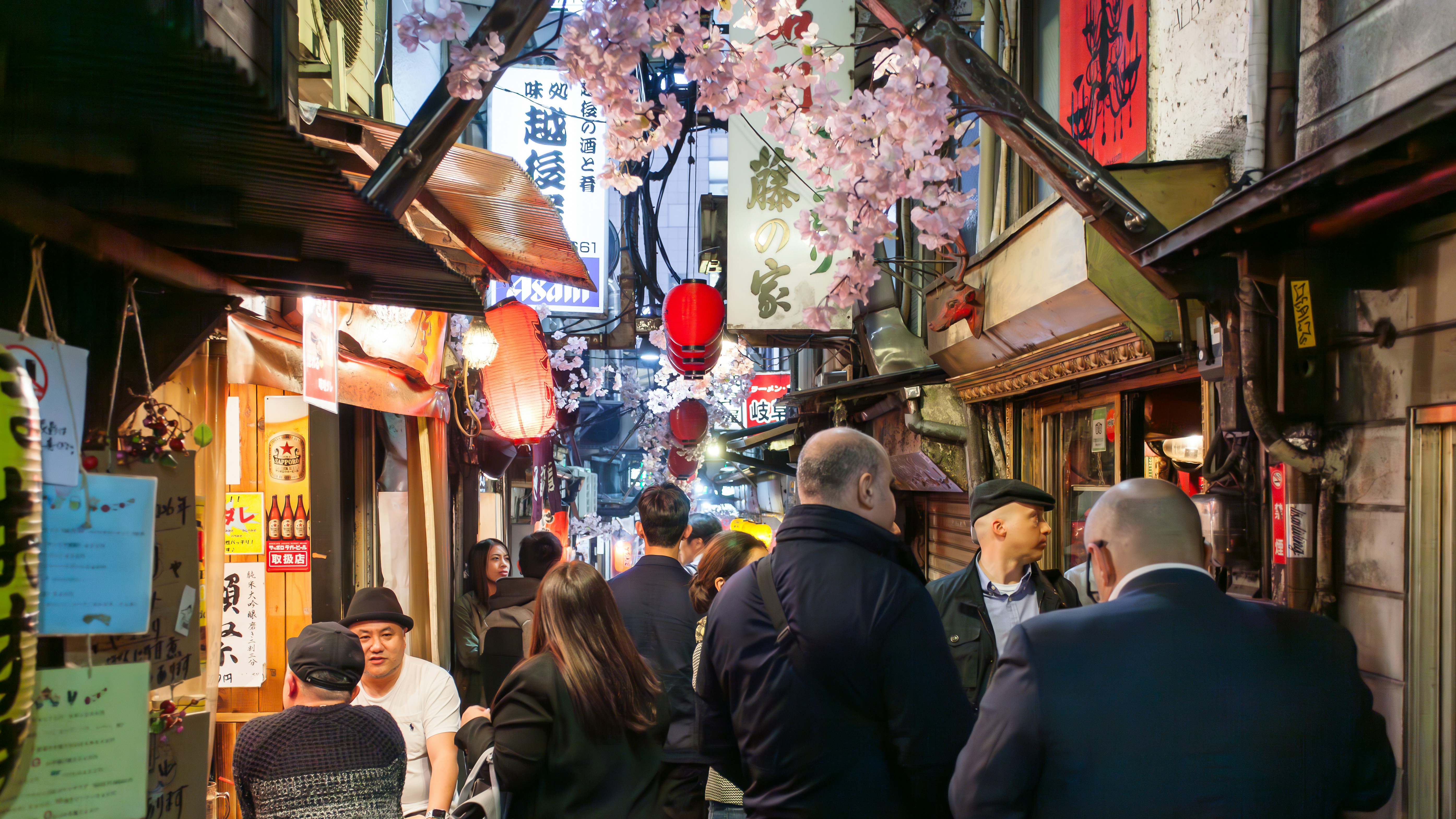 People walking down a narrow street with shops and lanterns.