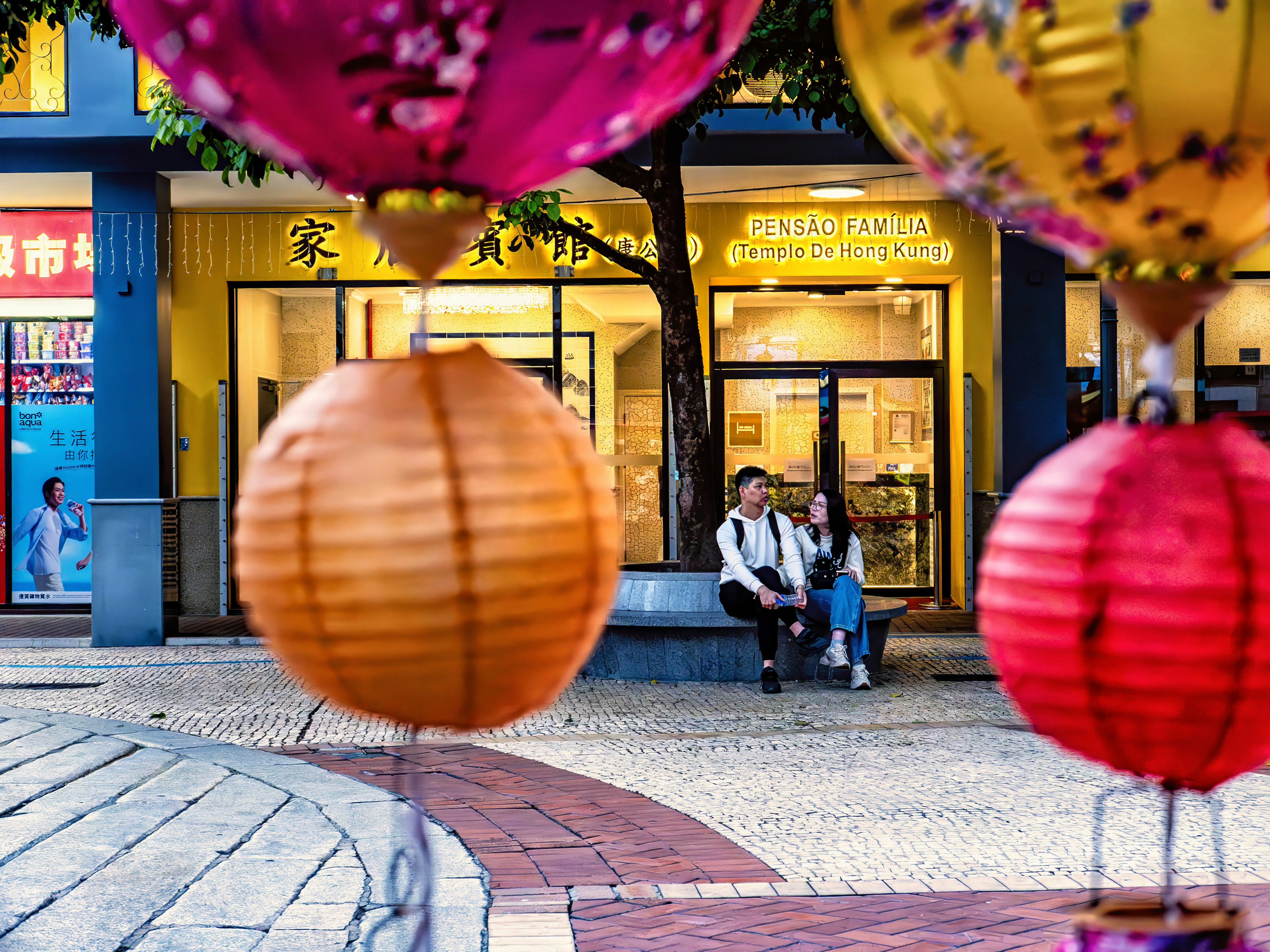 A couple sits on a bench near colorful lanterns.