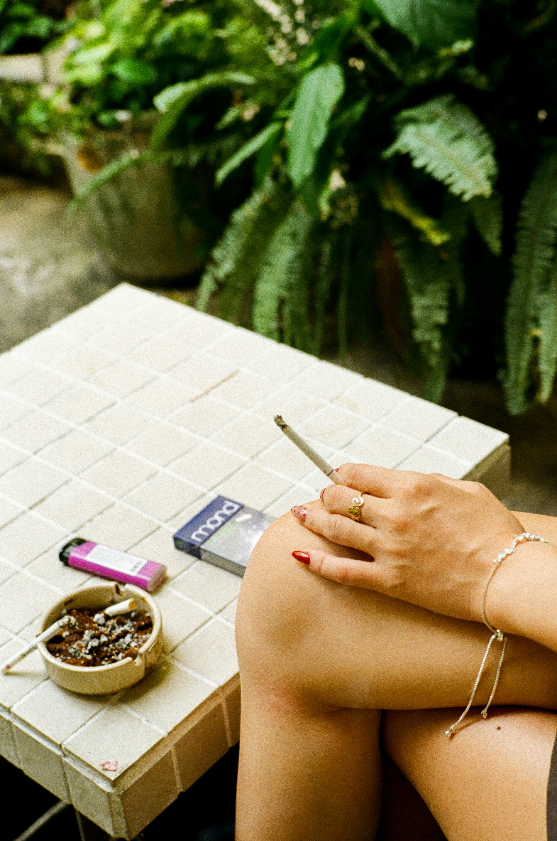 Woman holding cigarette with ashtray and lighter on table