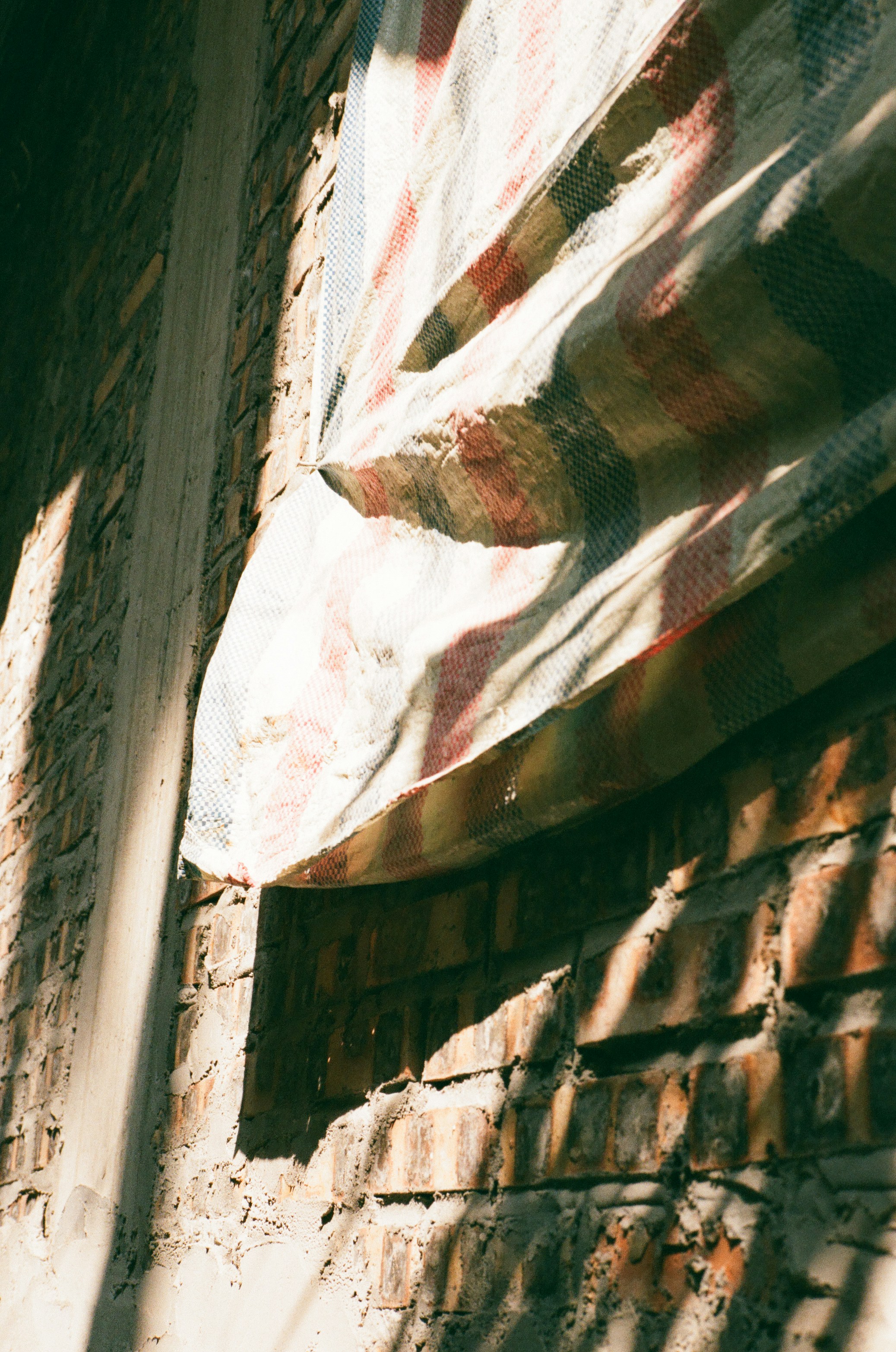 Striped tarp covers a brick wall with shadows