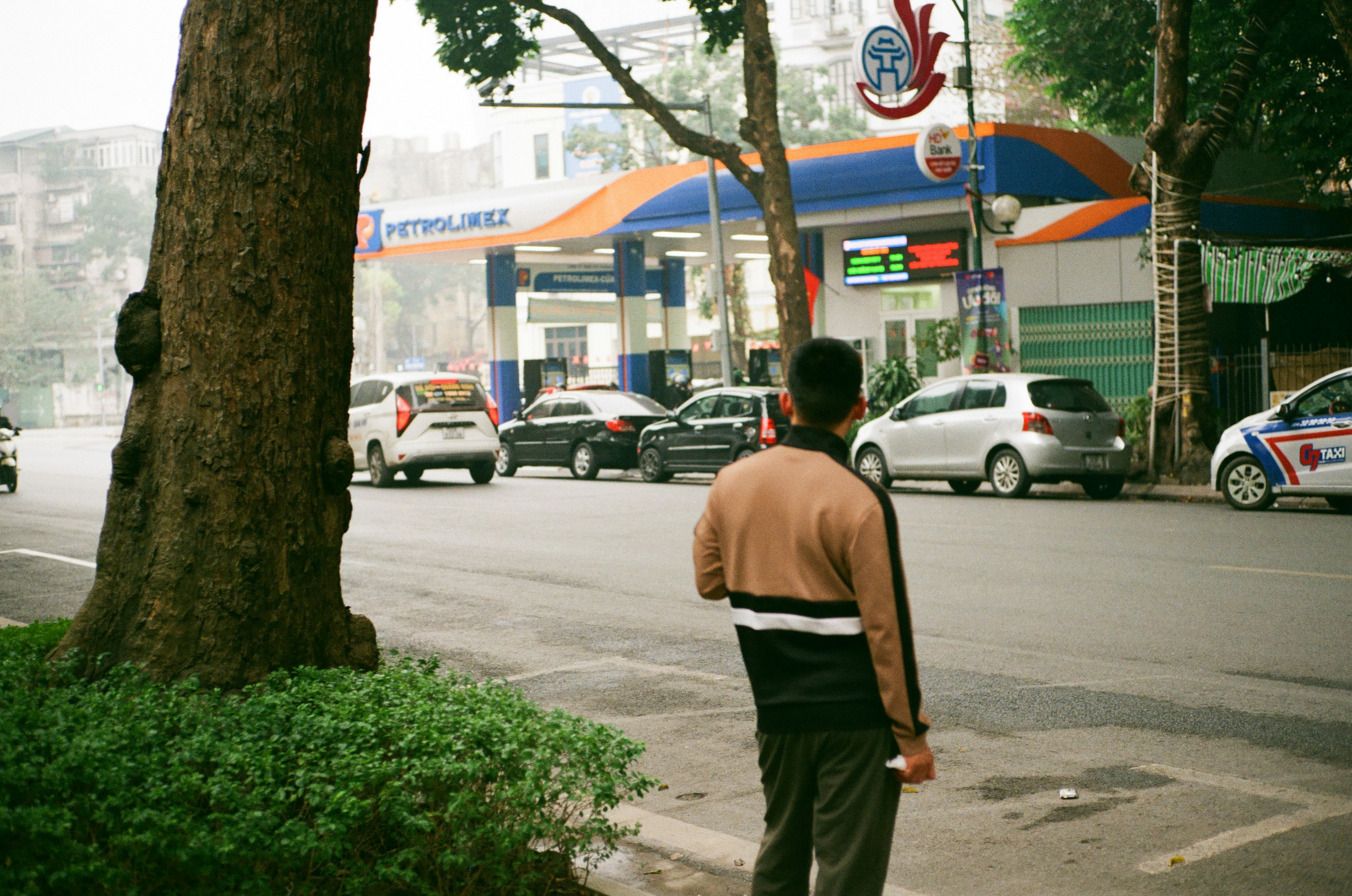 Pria berdiri di jalan dekat pompa bensin dengan mobil.