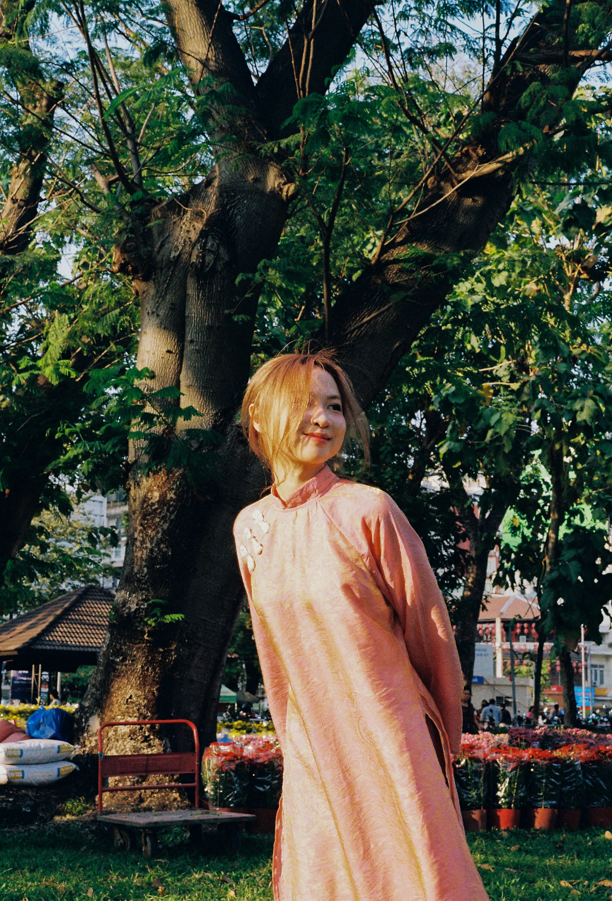 A woman in a pink dress stands in a park.
