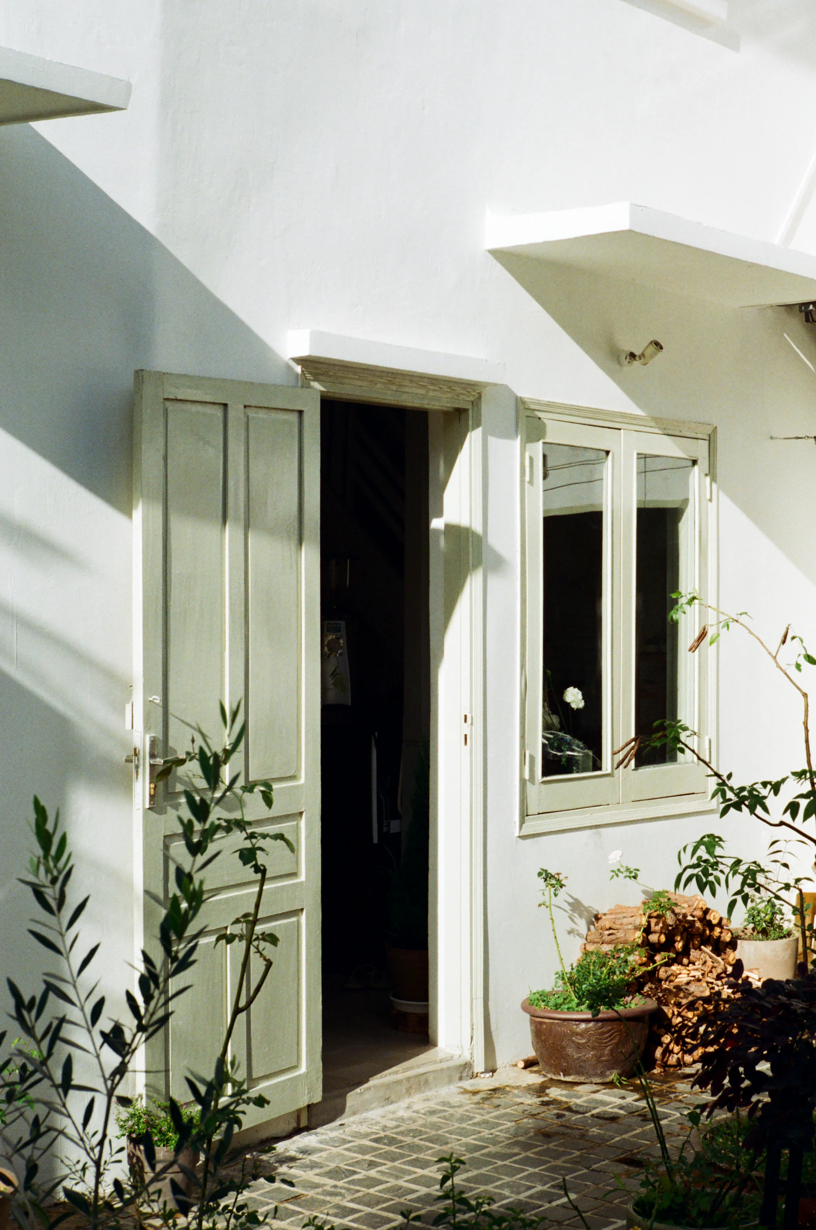 A sunlit white wall with an open doorway, its shutter folded back