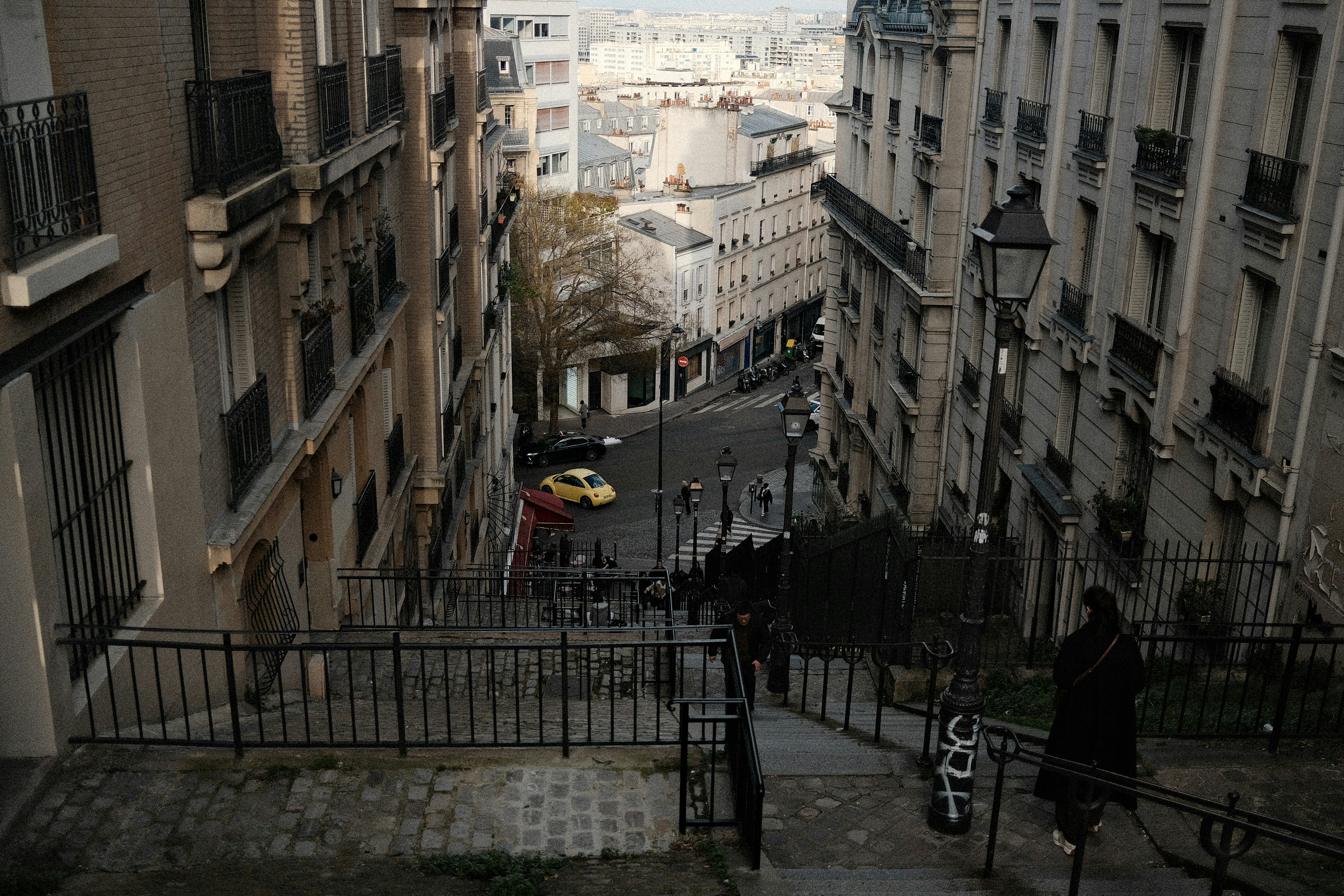 Rua íngreme com prédios e um carro amarelo abaixo.