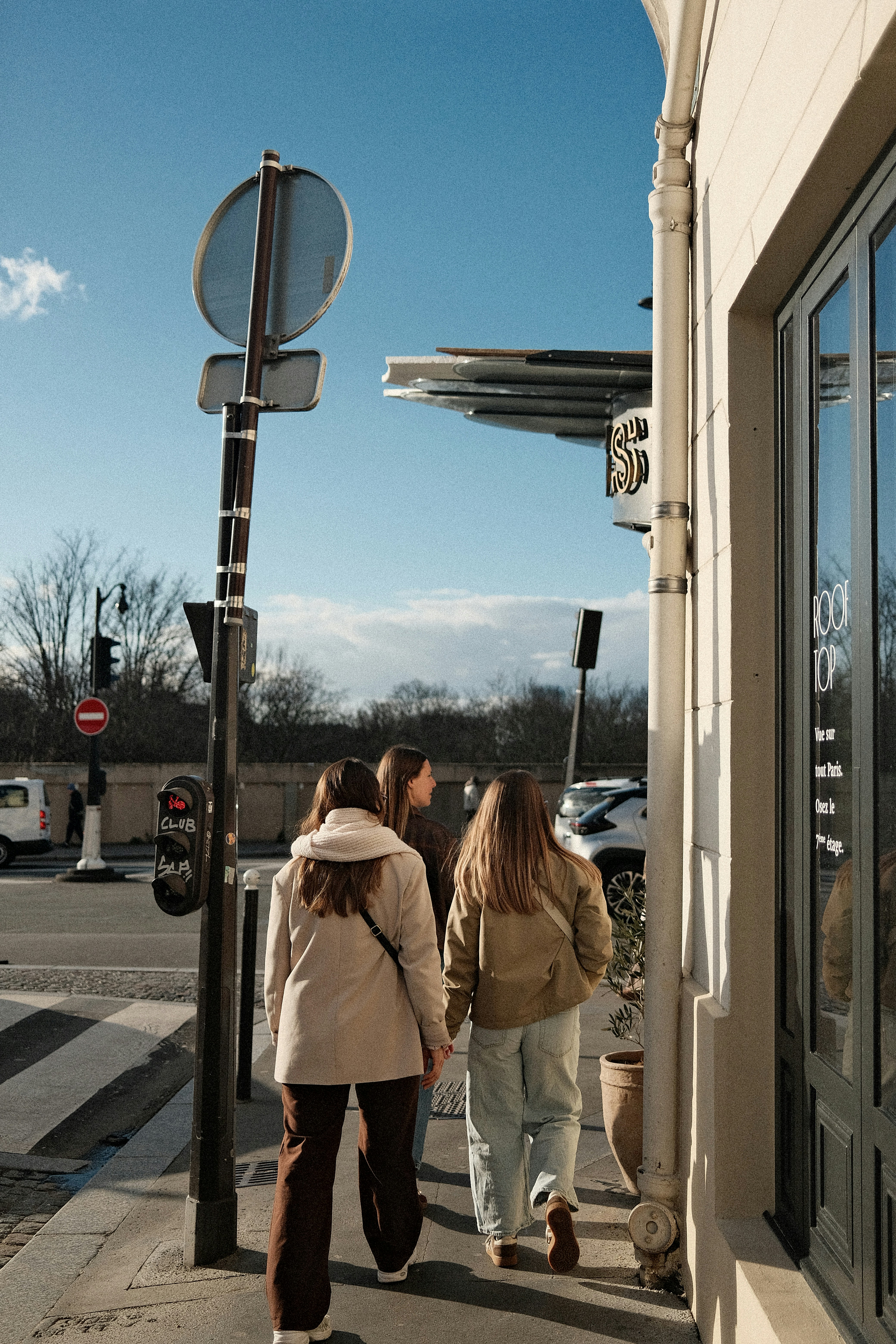 Três jovens caminham por uma rua ensolarada.