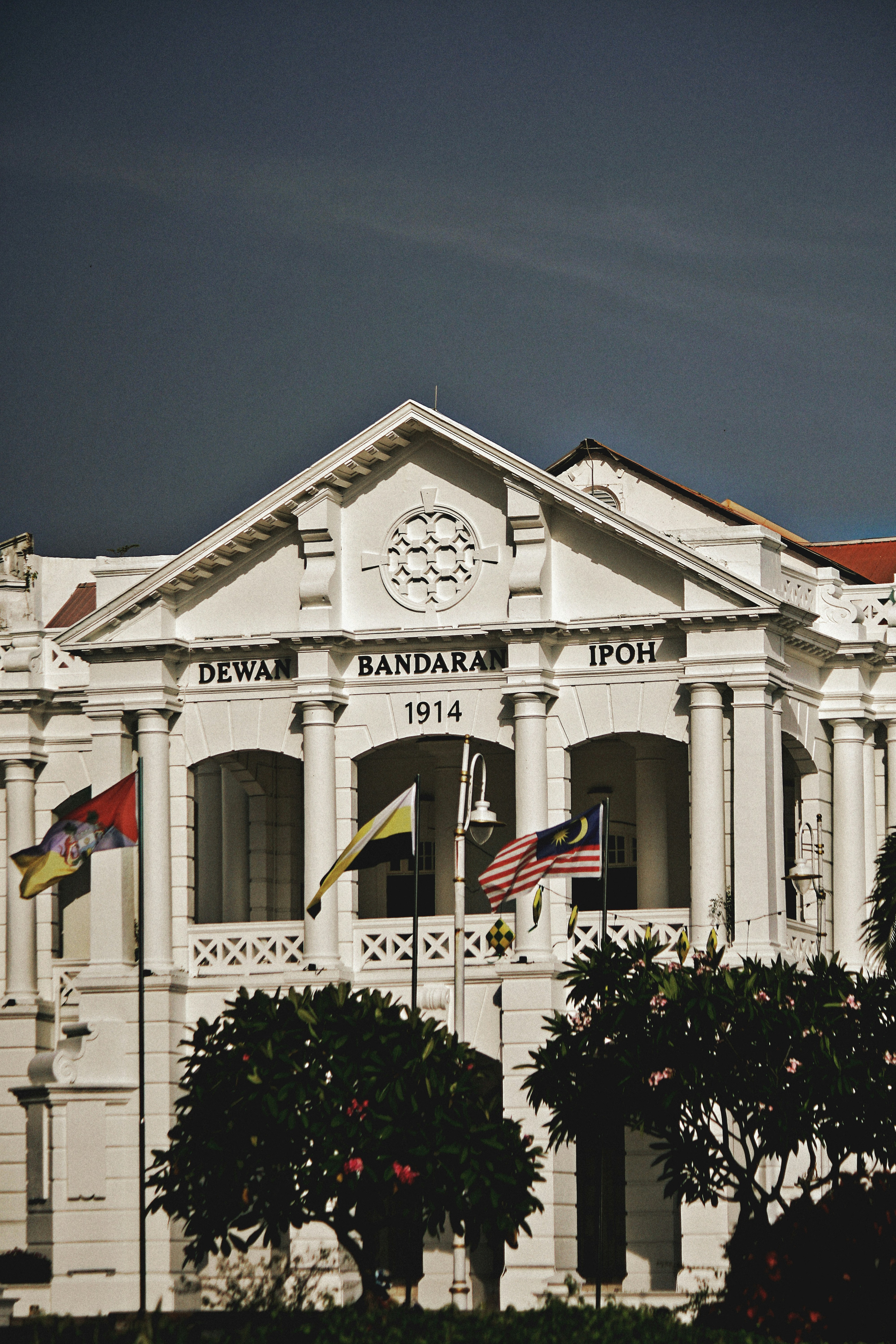 Bangunan kolonial putih dengan bendera dan pepohonan