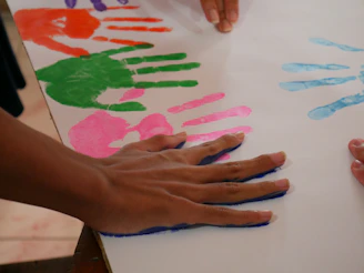 Colorful handprints on white paper with a hand pressing down.