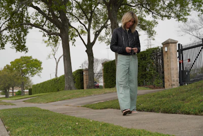 Woman walking on a sidewalk near a fence.