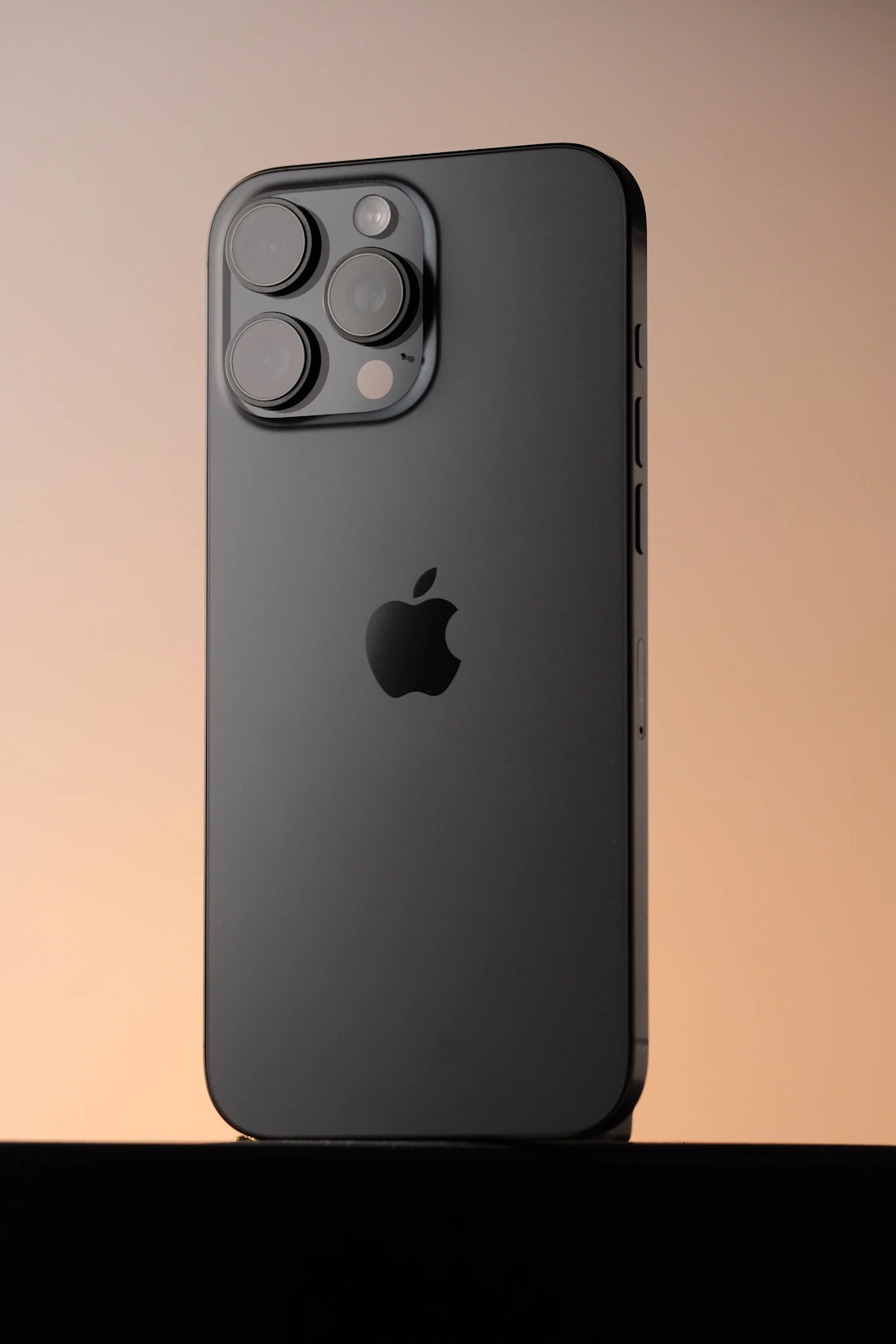 Dark grey iPhone Pro standing against a warm sunset gradient