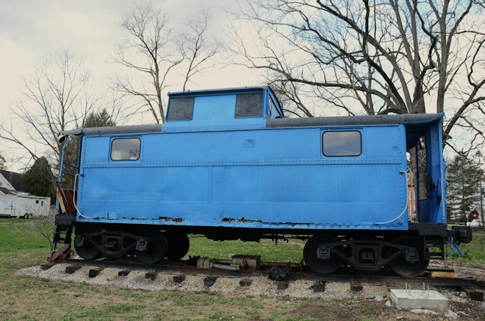 Bright blue caboose resting on railroad tracks outside a museum