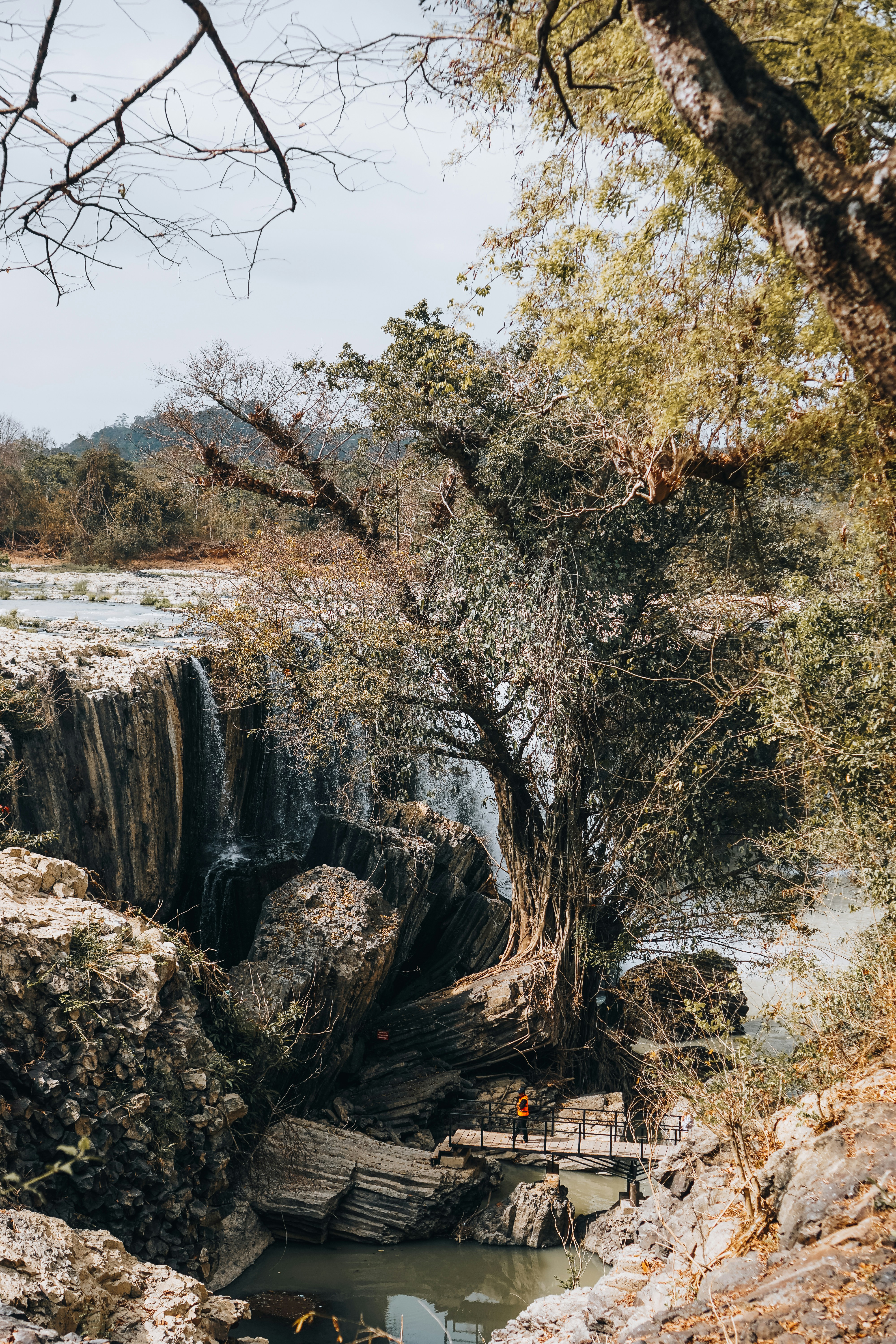 Zwei Personen überqueren eine Holzbrücke in der Nähe eines Wasserfalls.