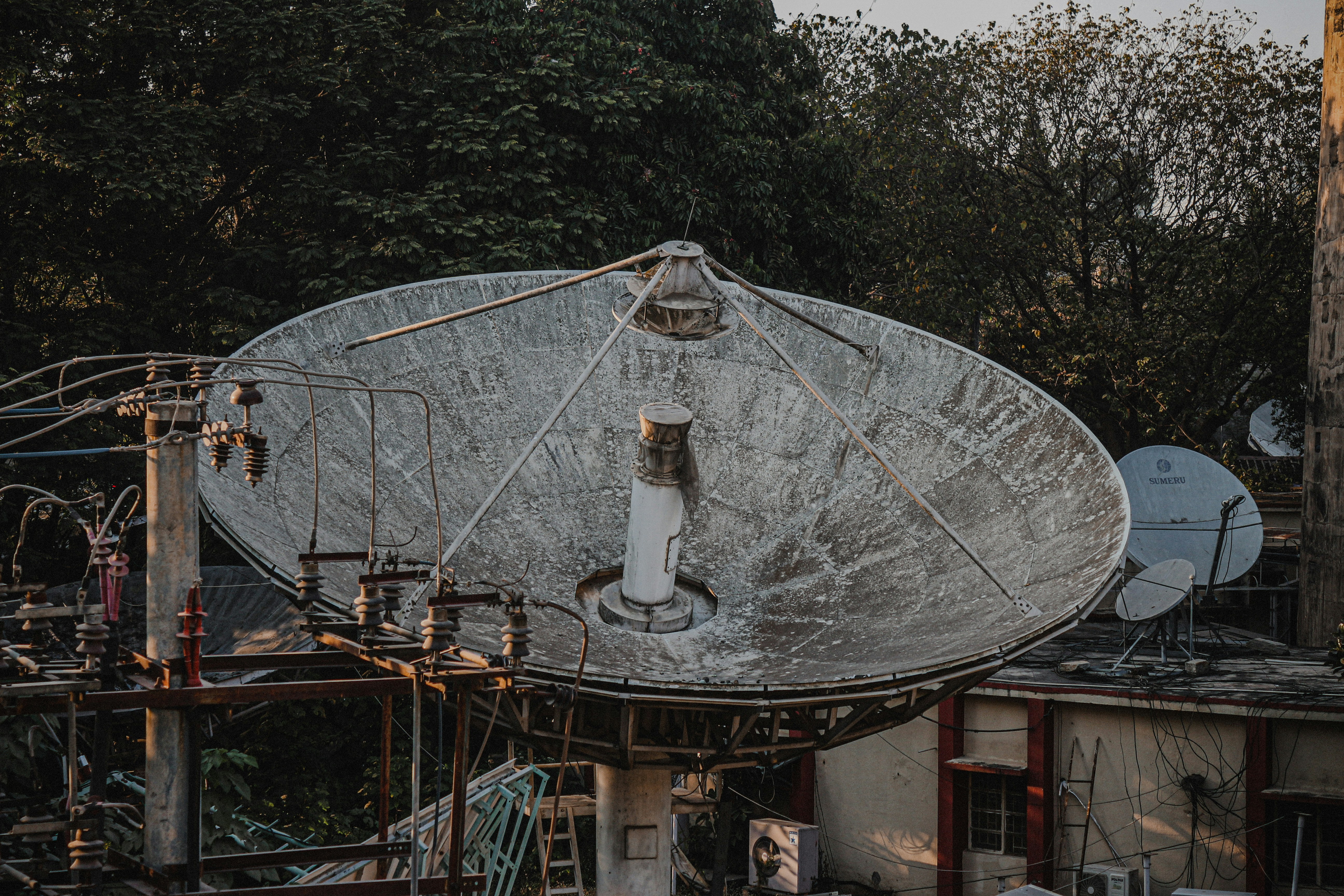 Large satellite dish antenna on rooftop with trees behind