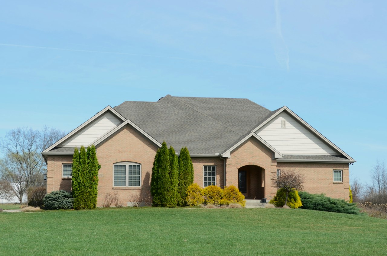 Brick single-story home with a mowed green lawn and clear blue sky in spring