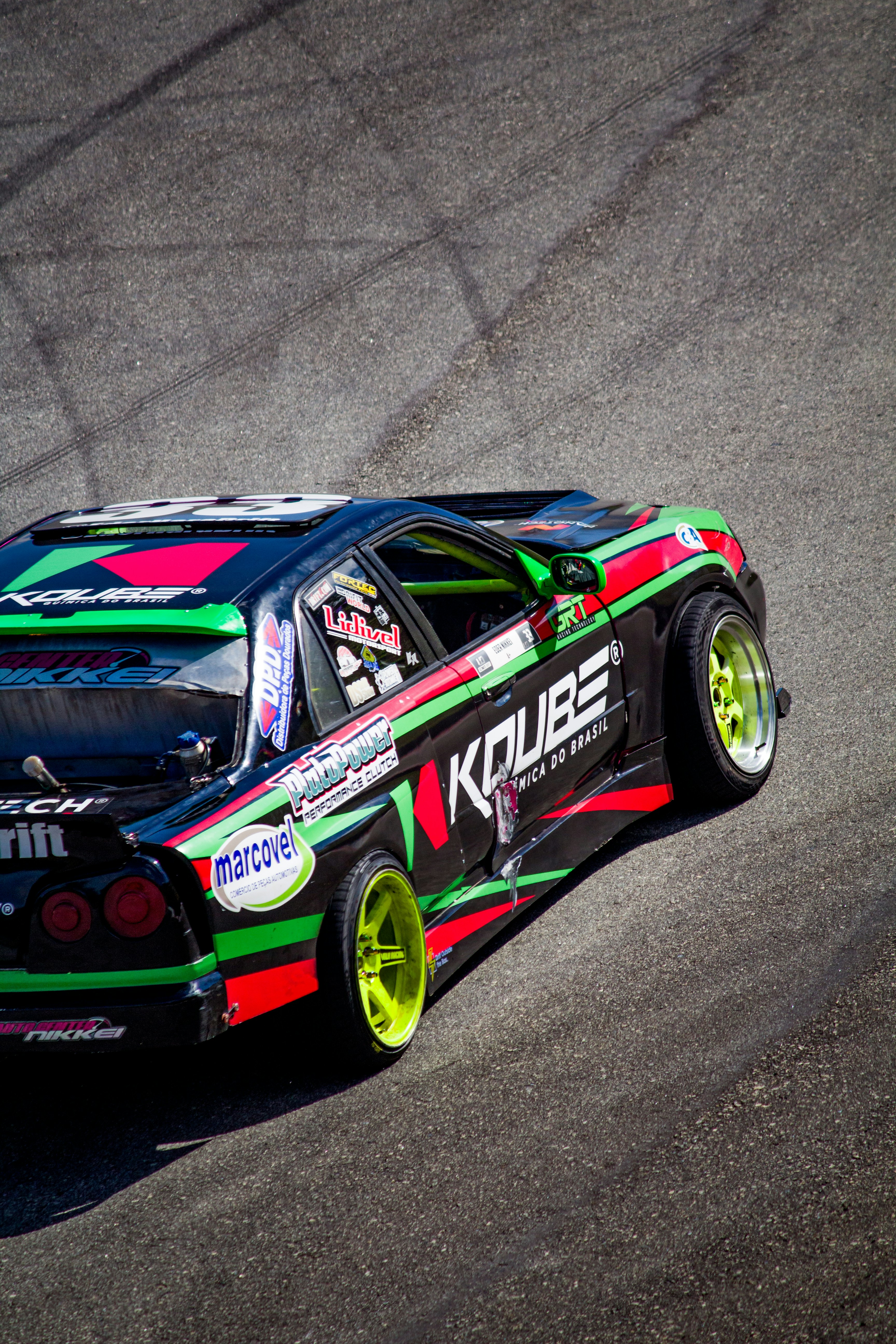 Mobil drift hitam dengan garis-garis balap warna-warni di trek