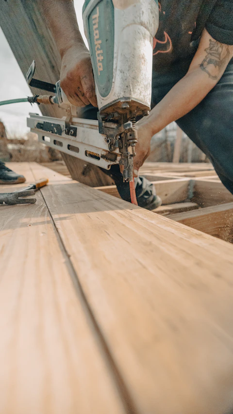 Construction worker using a nail gun on wooden planks.