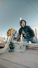 Man using a miter saw outdoors on a wooden deck.