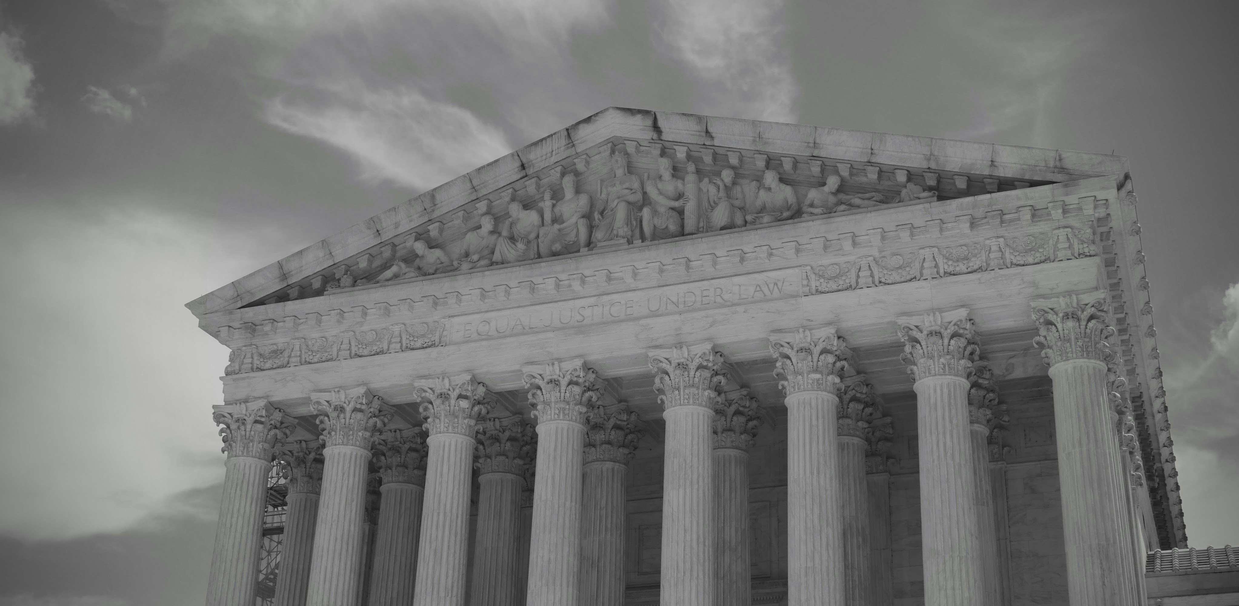 Grand neoclassical building with columns against cloudy sky.
