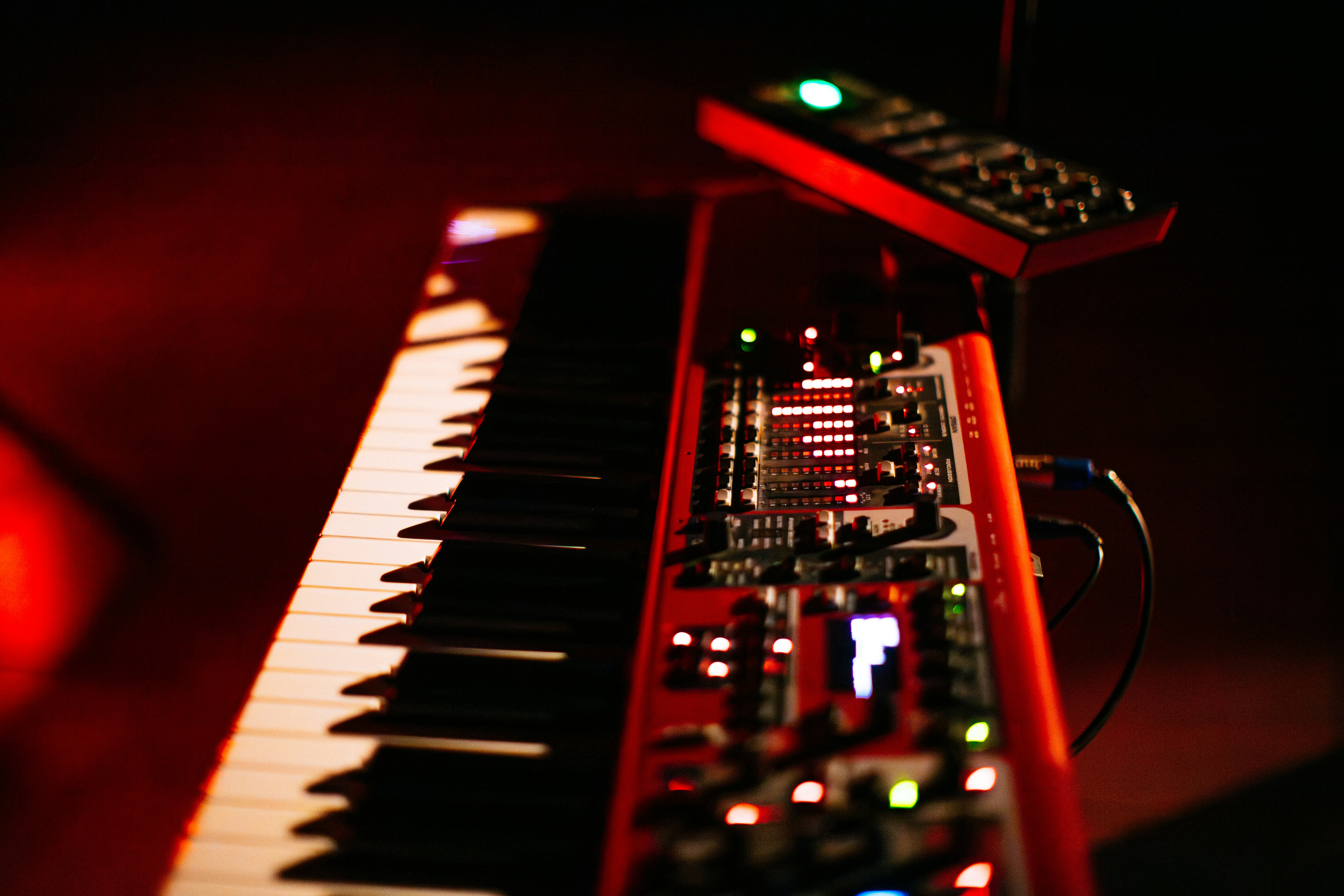Close-up of a red synthesizer keyboard with glowing controls and keys under dramatic red lighting. A music production setup prepared for a live performance or recording session.