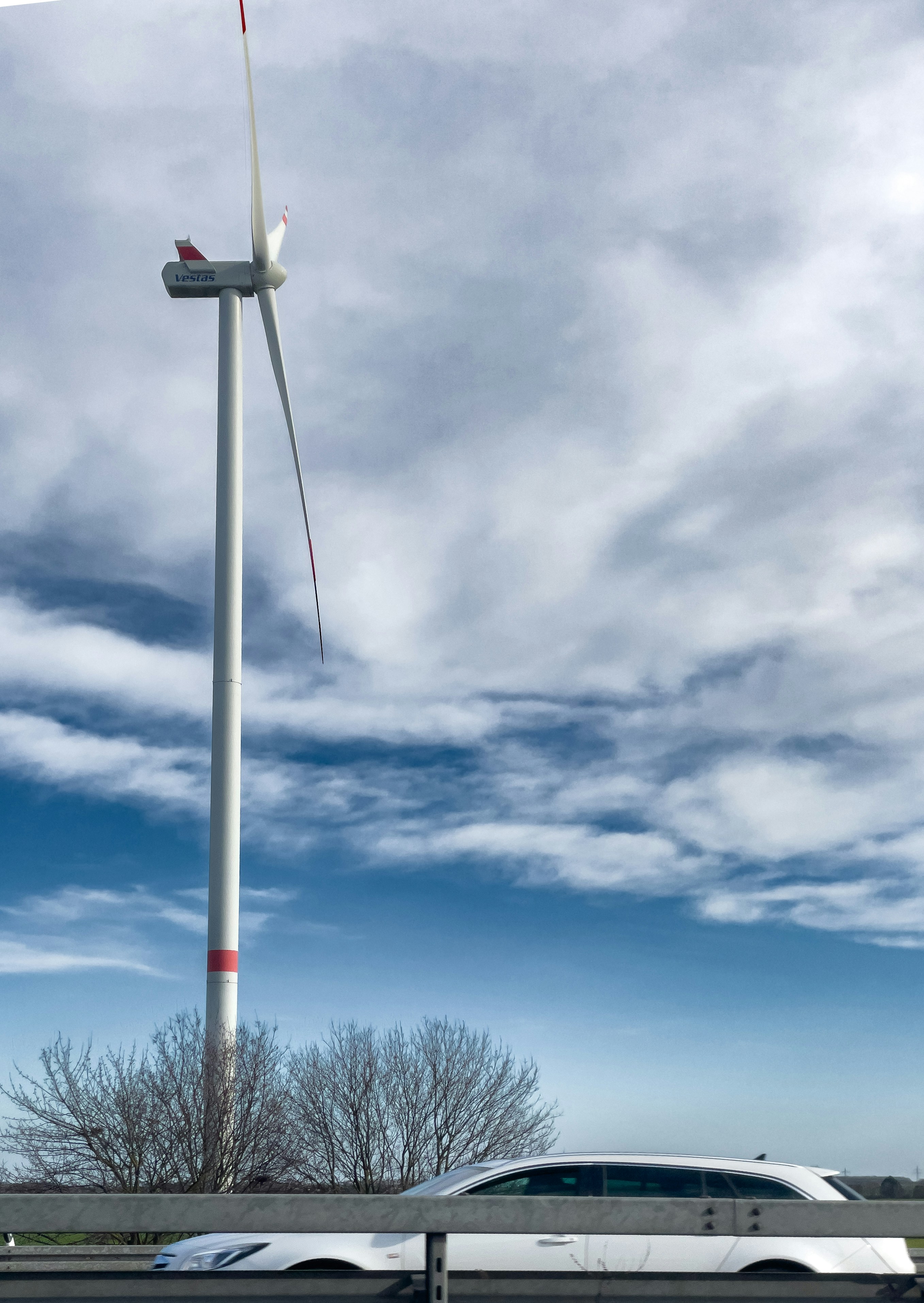 Um carro branco passa por uma turbina eólica alta.