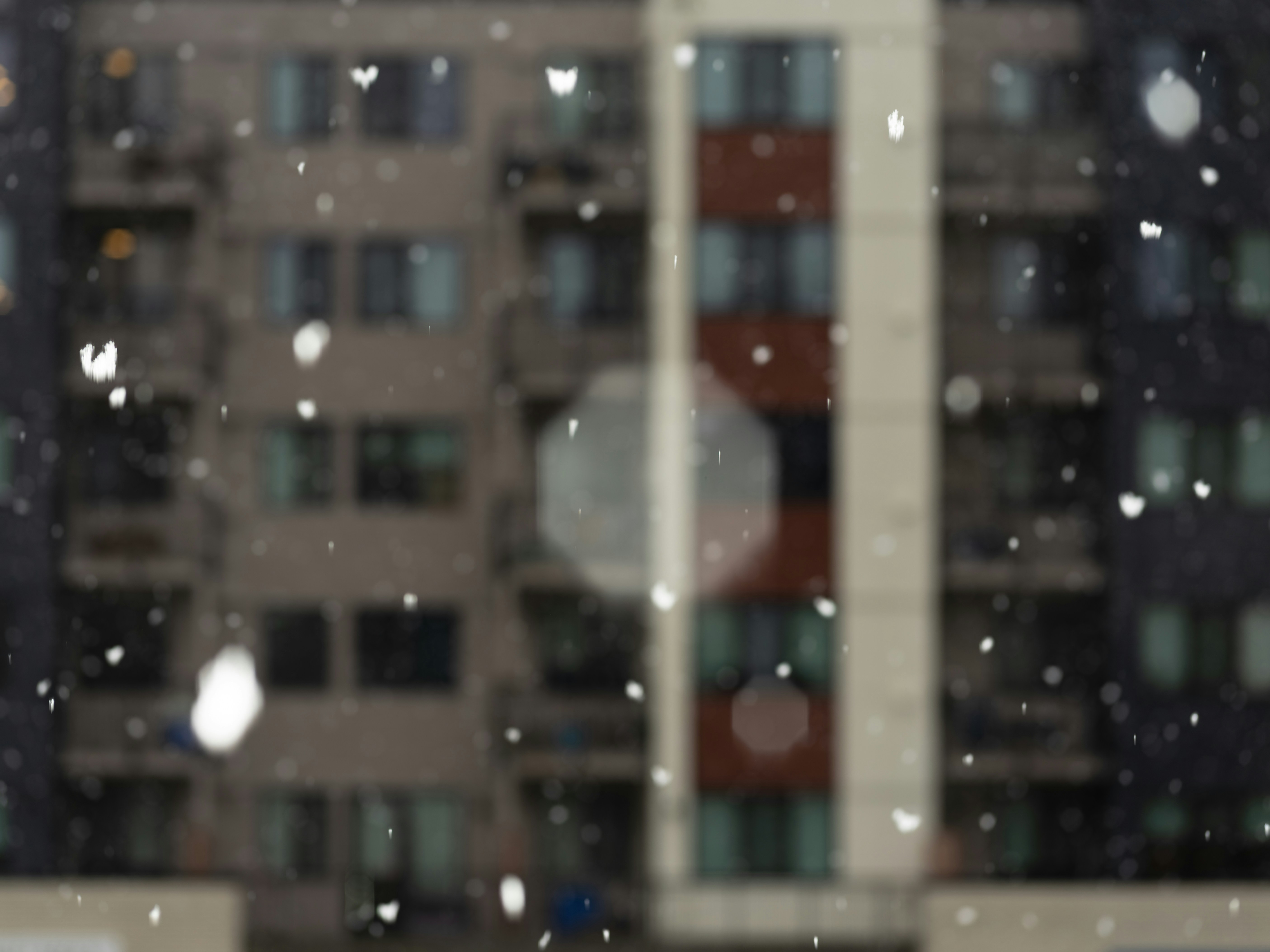 Schnee fällt vor einem verschwommenen Wohnhaus.