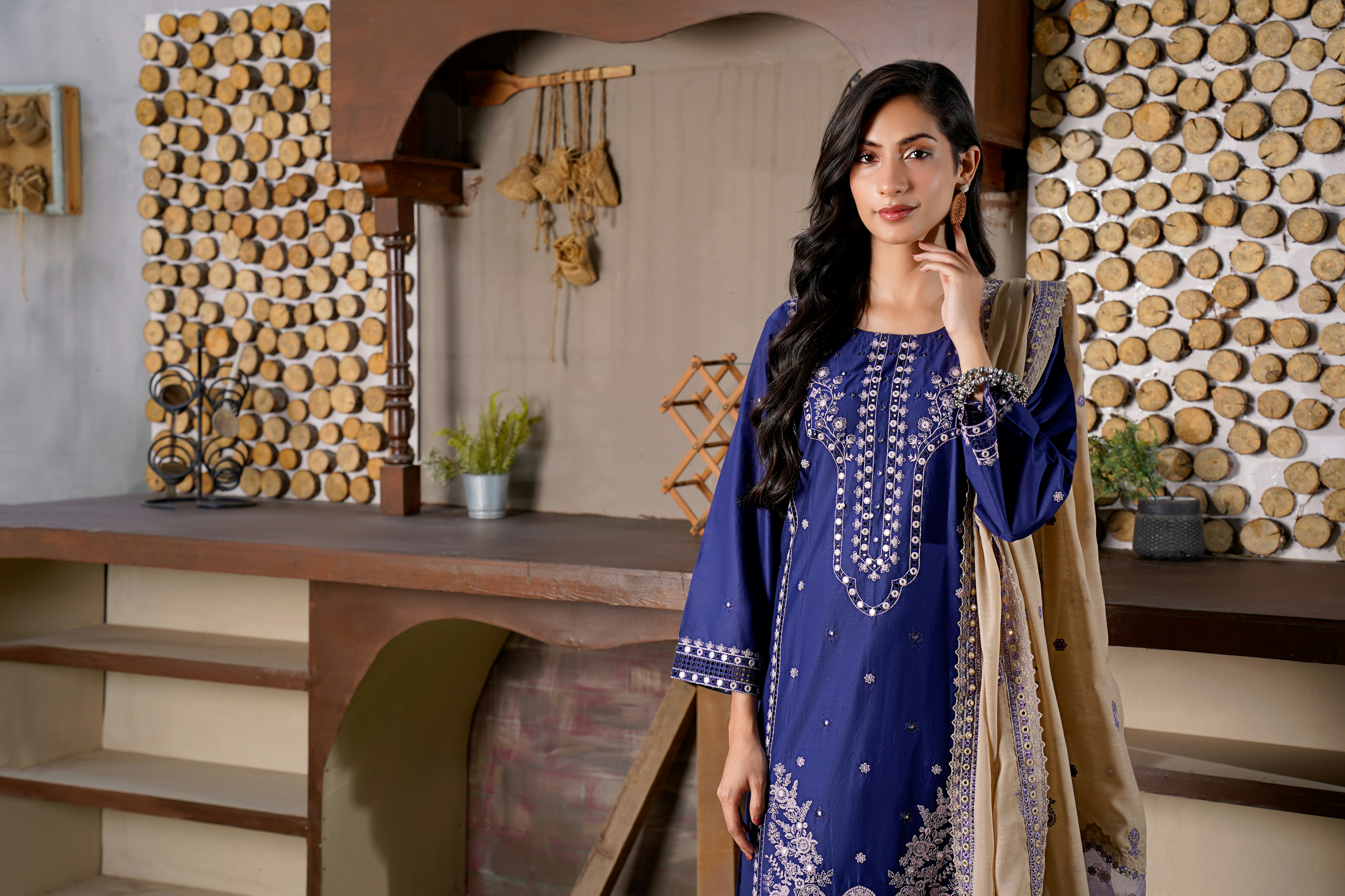Woman in a blue embroidered dress with a tan shawl.
