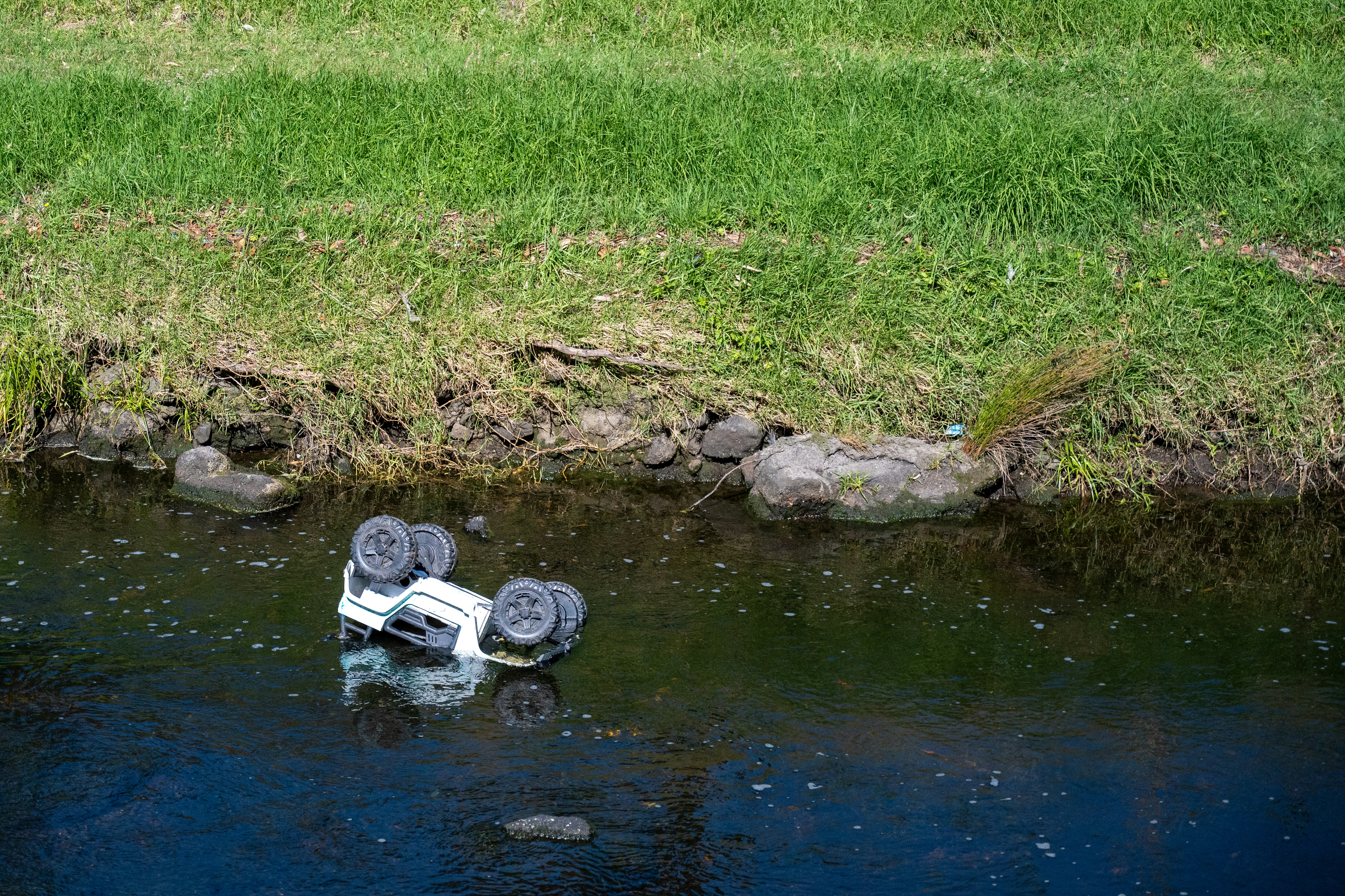 A toy truck lies overturned in a shallow stream.
