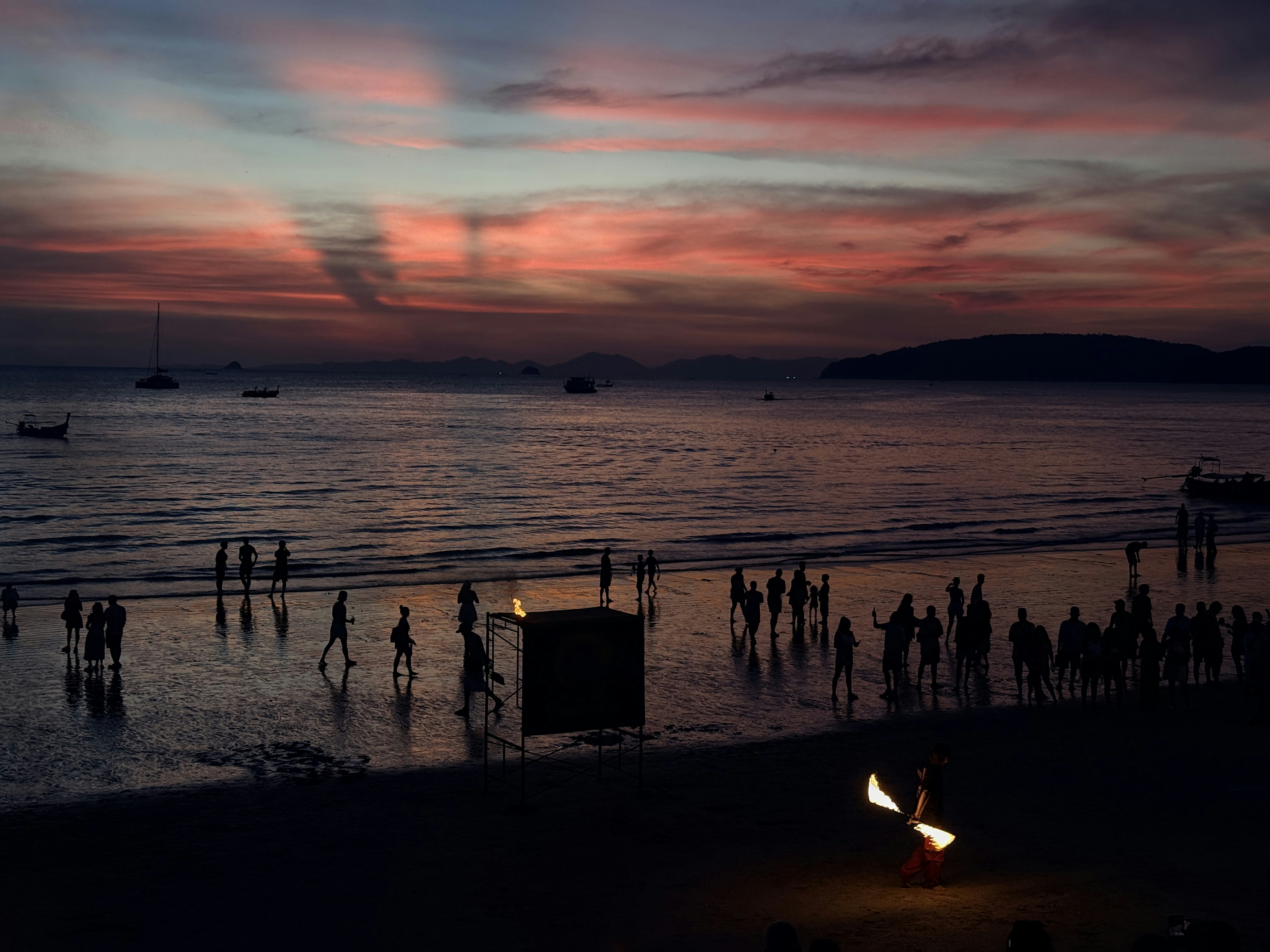 People on a beach at sunset with a fire dancer.