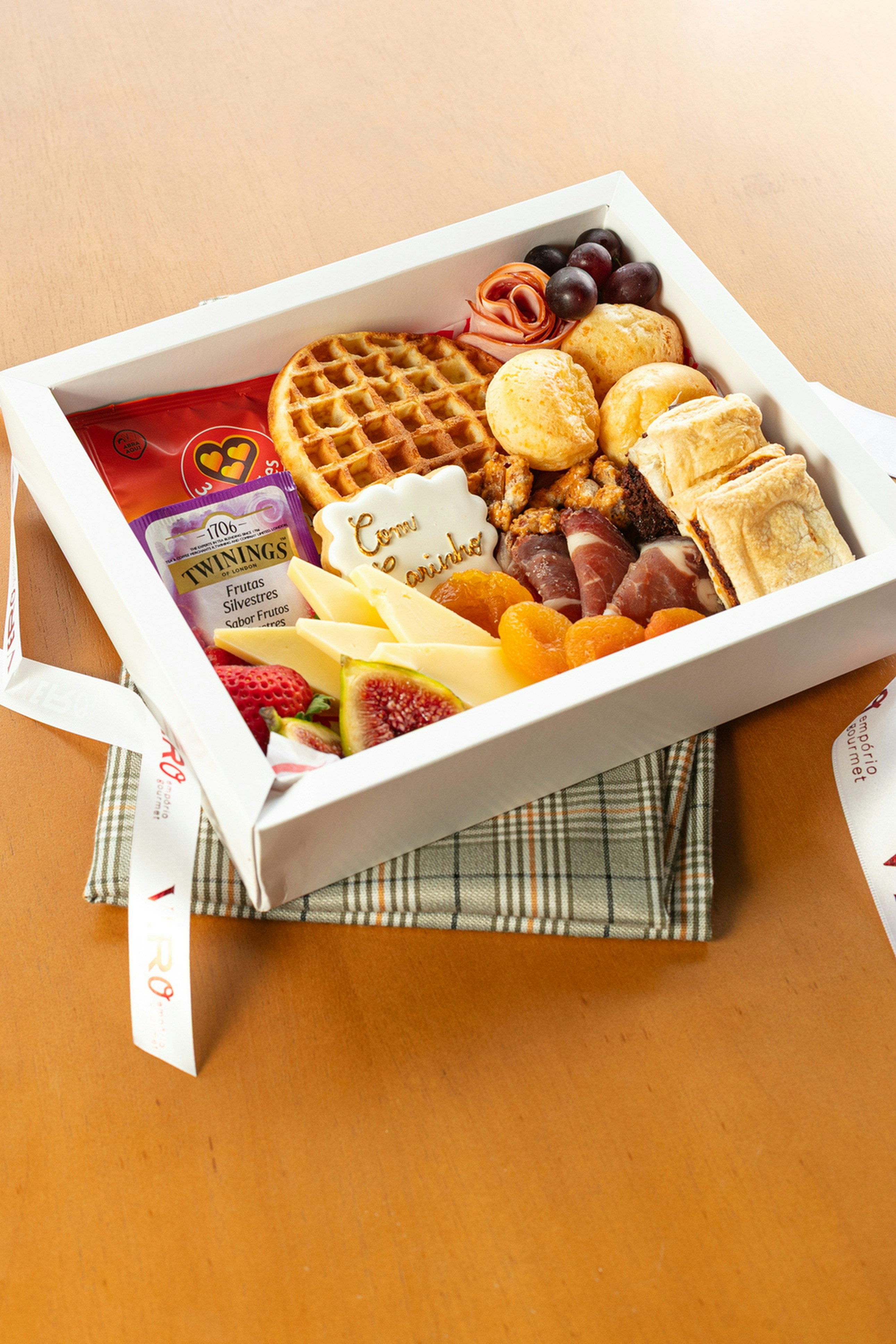 A white box filled with cheese, fruit, waffles, and snacks.