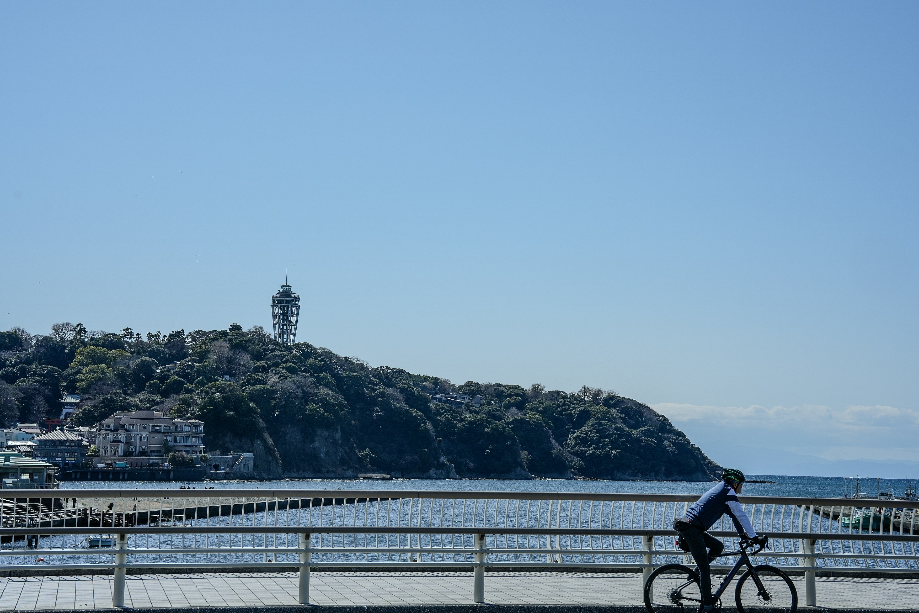 Cyclist on a bridge with a lighthouse on a hill.